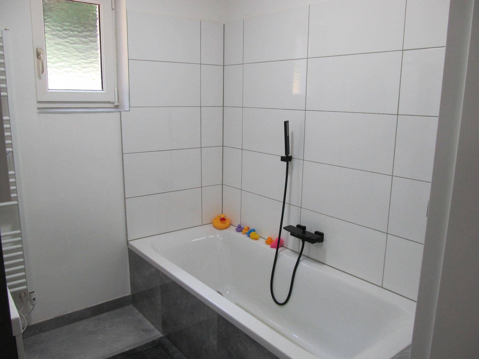 Badezimmer mit Badewanne, Duscharmatur und Fenster für natürliche Belüftung.