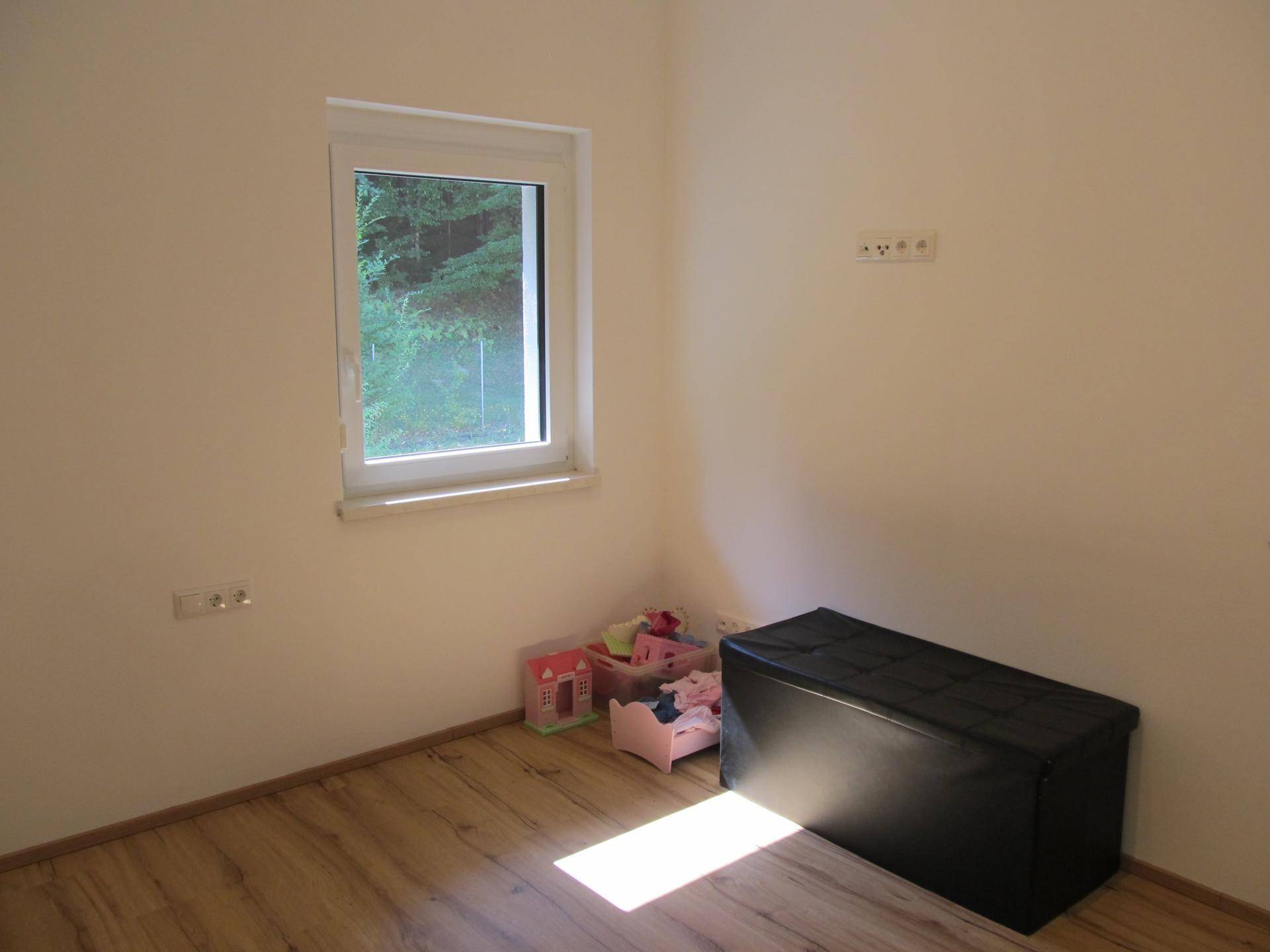 Kleines, helles Zimmer mit Holzfußboden und Blick ins Grüne, geeignet als Kinder- oder Gästezimmer.