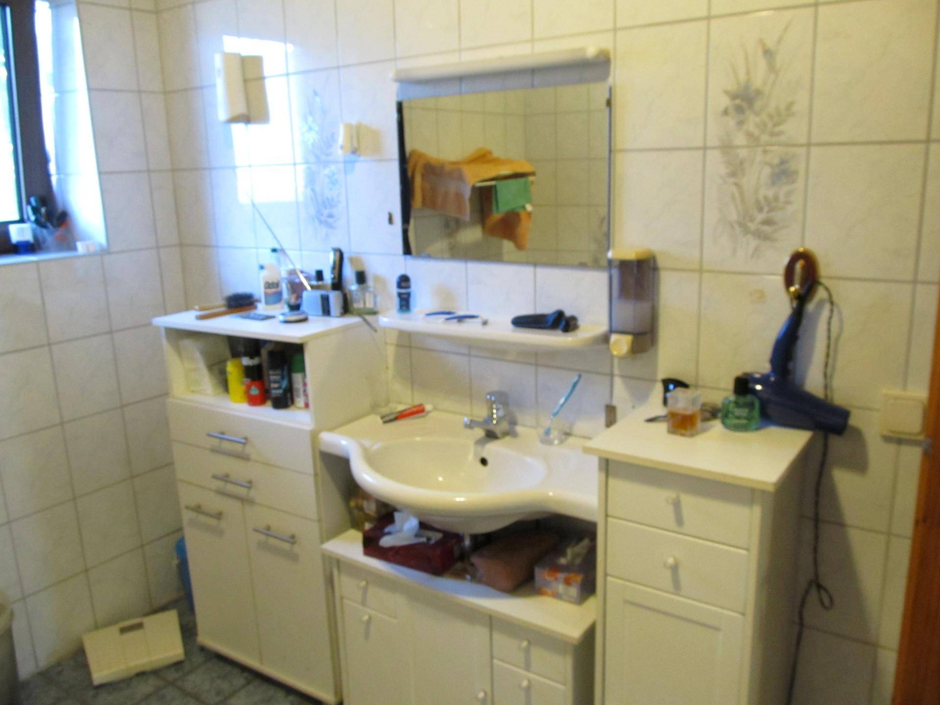 Badezimmer mit Einzelwaschbecken, Spiegelschrank und weißen Fliesen, gut beleuchtet.