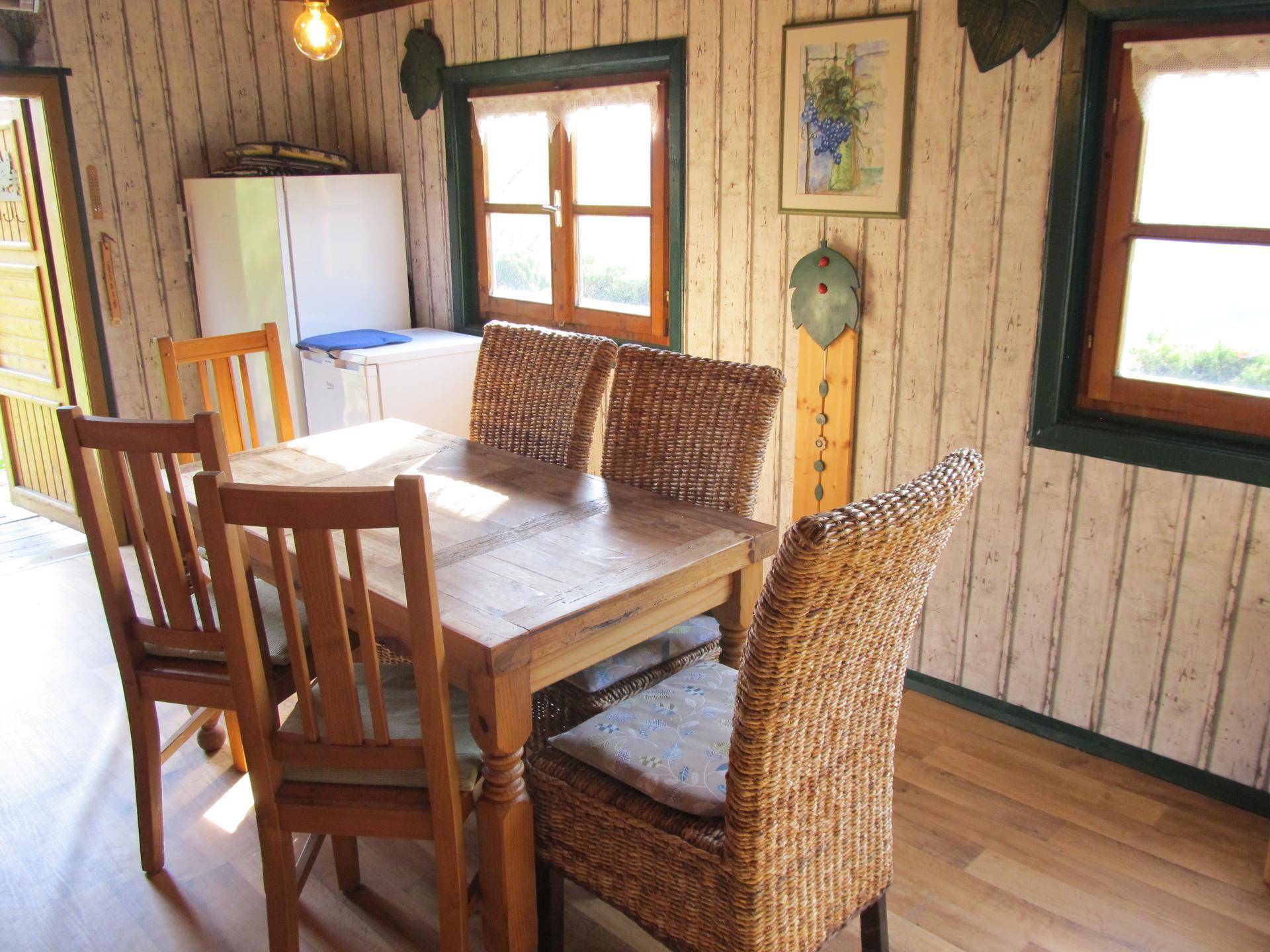 Heller Essbereich mit Holztisch und Korbstühlen, angrenzend an einen Küchenbereich mit Kühlschrank.