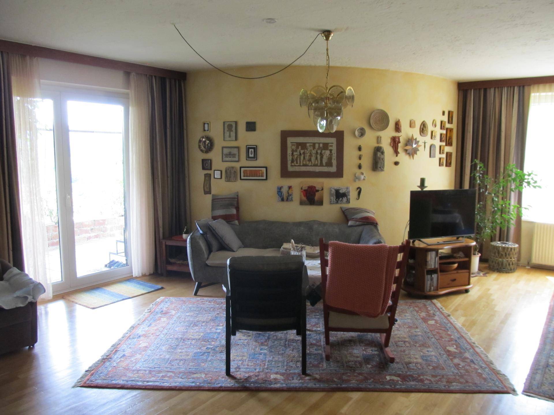 Gemütliches Wohnzimmer mit Holzboden, vielen Bildern an der Wand und Zugang zur Terrasse.