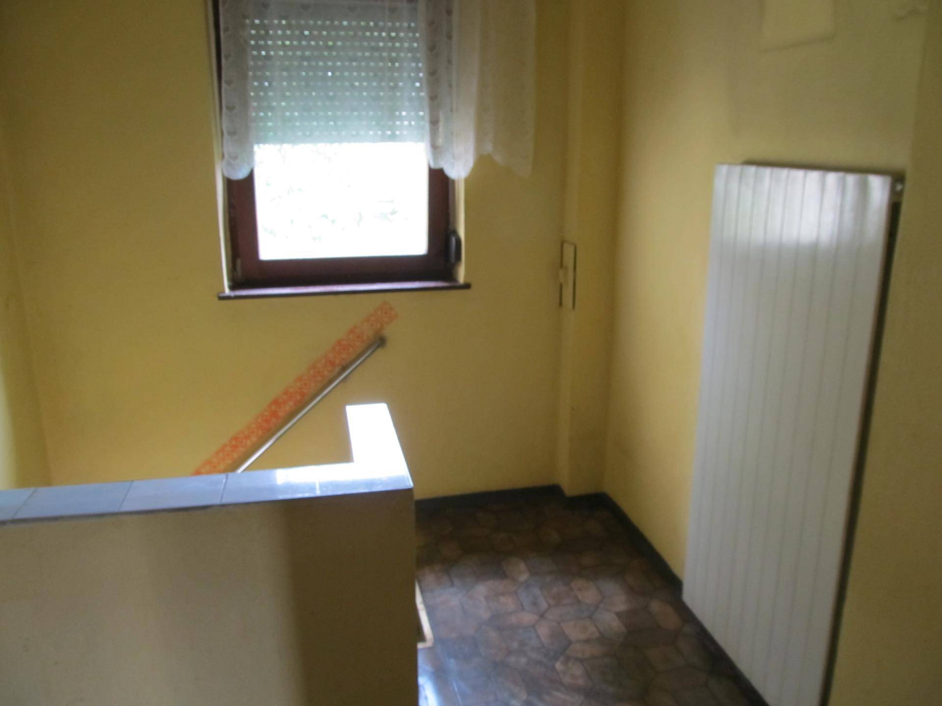Heller Flurbereich mit gelben Wänden, einem Fenster und einem Heizkörper, der zu einer Treppe führt.