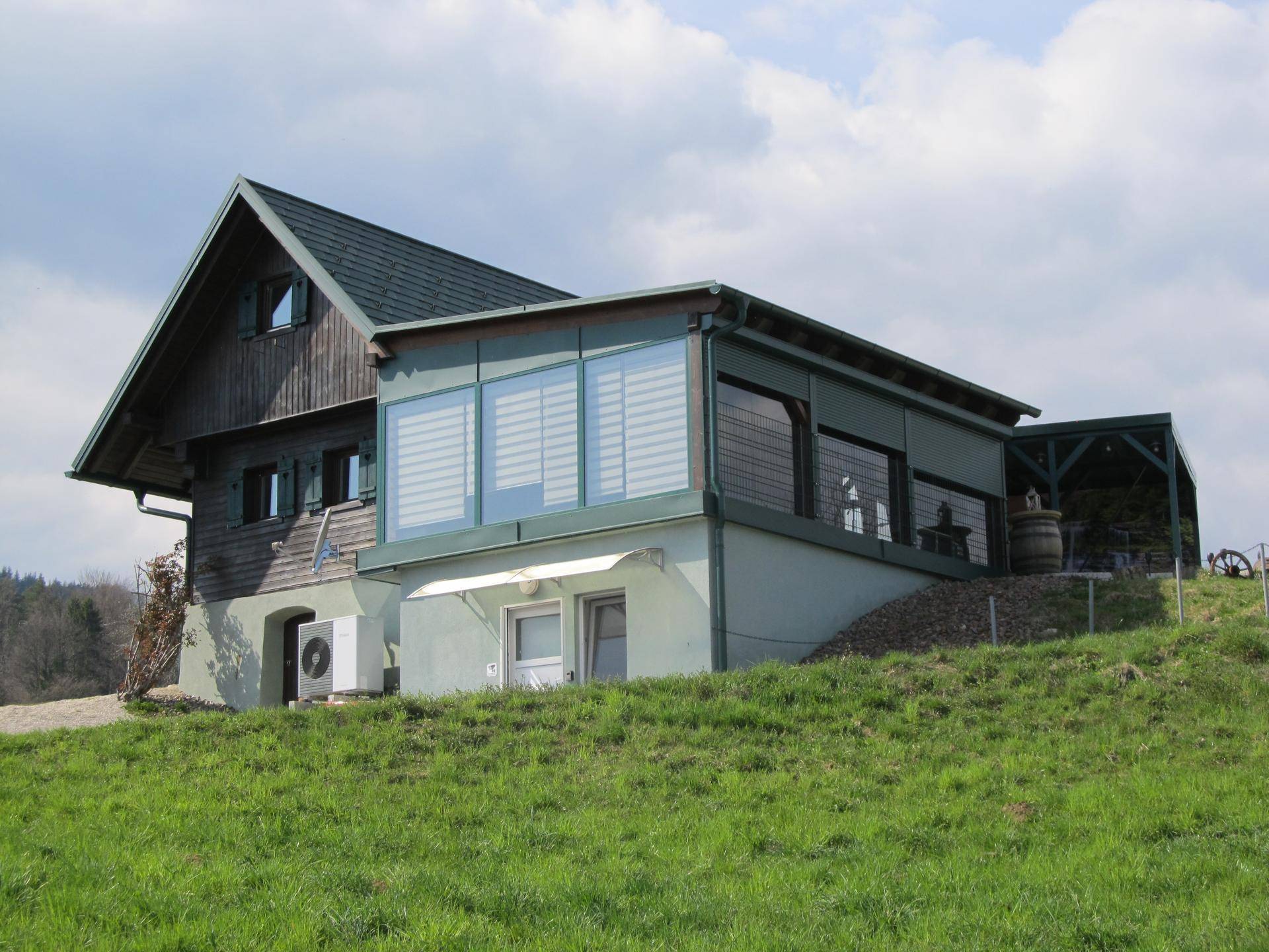 Ländliches Wohnhaus mit grünem Dach und Anbau auf einem grasbewachsenen Hügel.