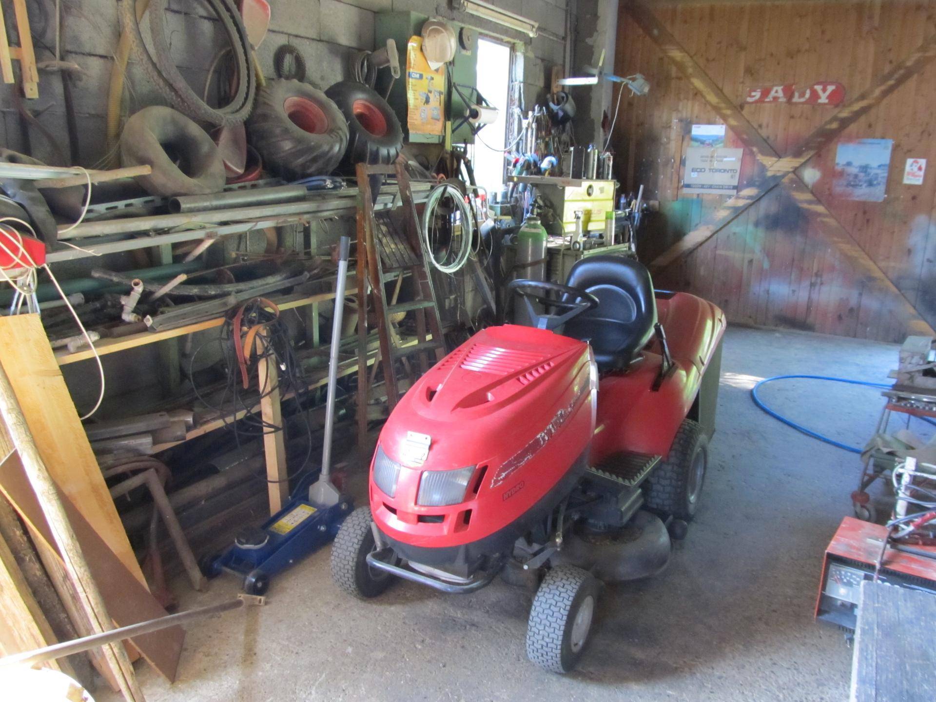 Garage oder Werkstatt mit einem roten Rasenmäher-Traktor und verschiedenen Geräten.