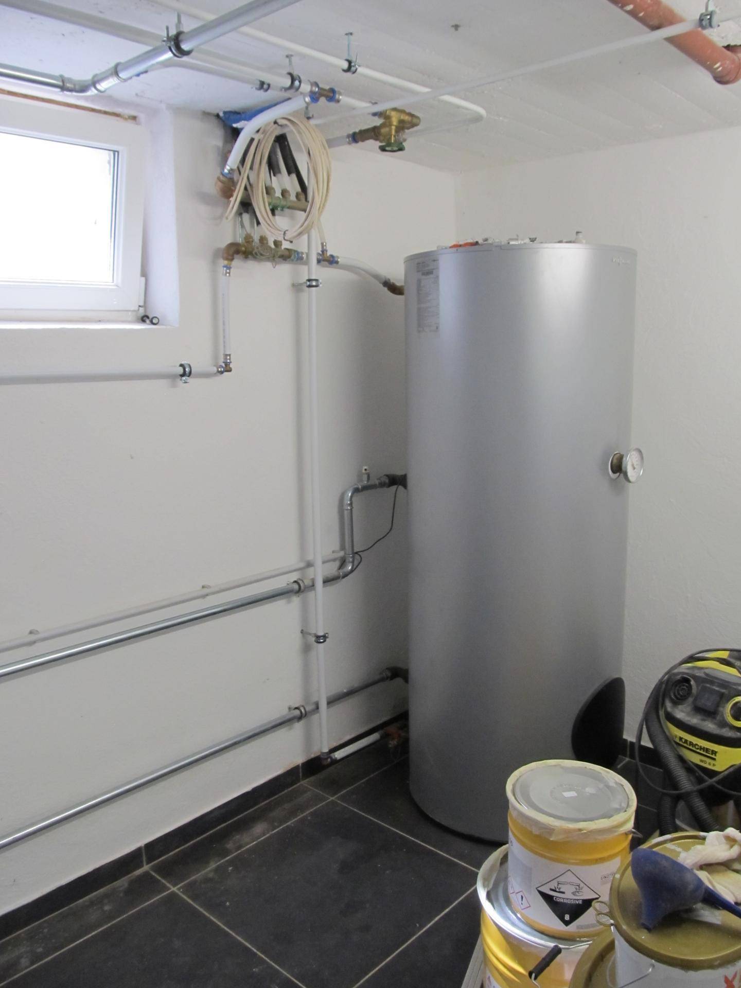 Technikraum mit großem Warmwasserspeicher, Fenster und sichtbaren Installationen an Wänden und Decke.