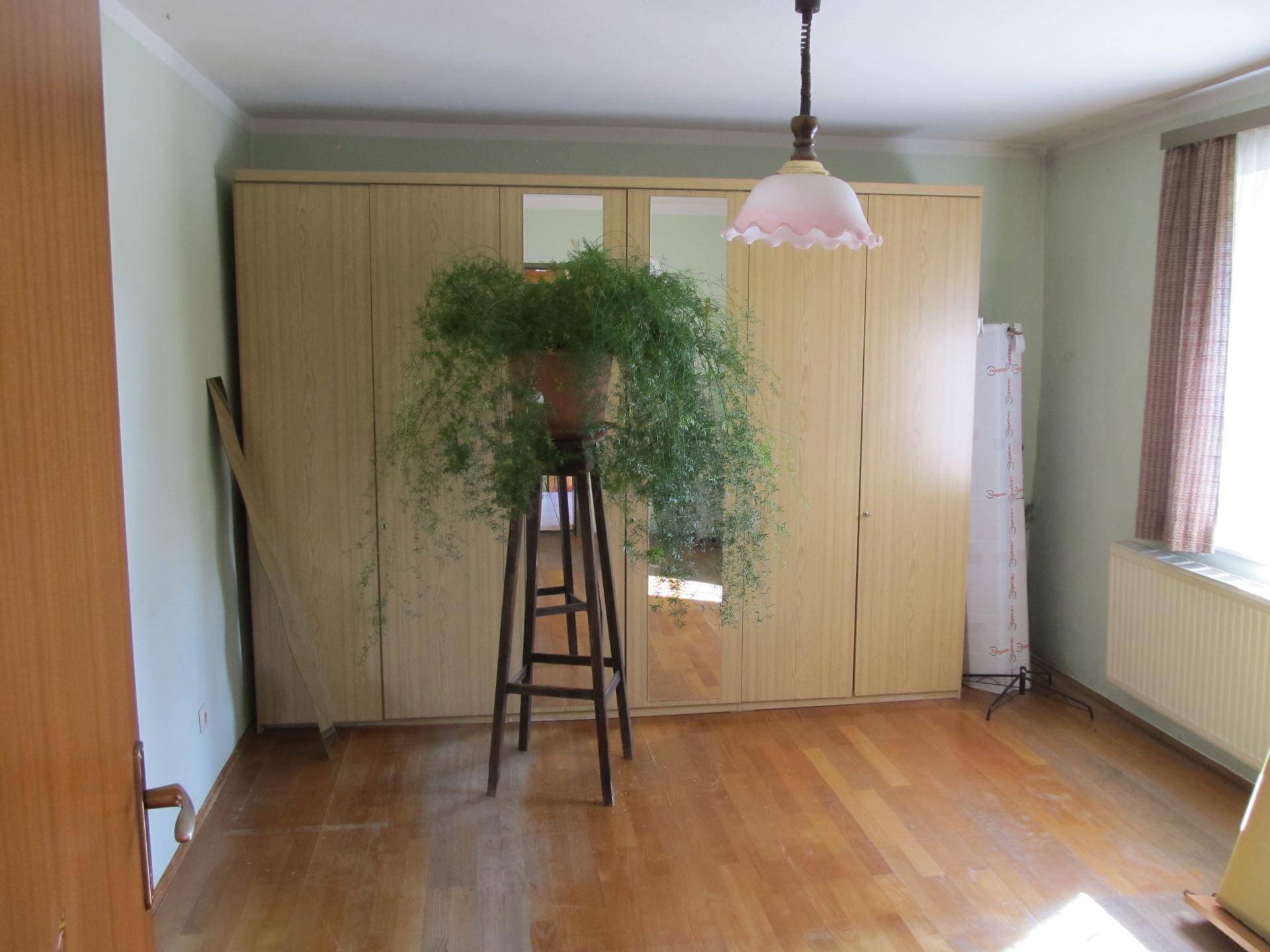 Geräumiges Schlafzimmer mit großem Kleiderschrank, Parkettboden und Fenster.