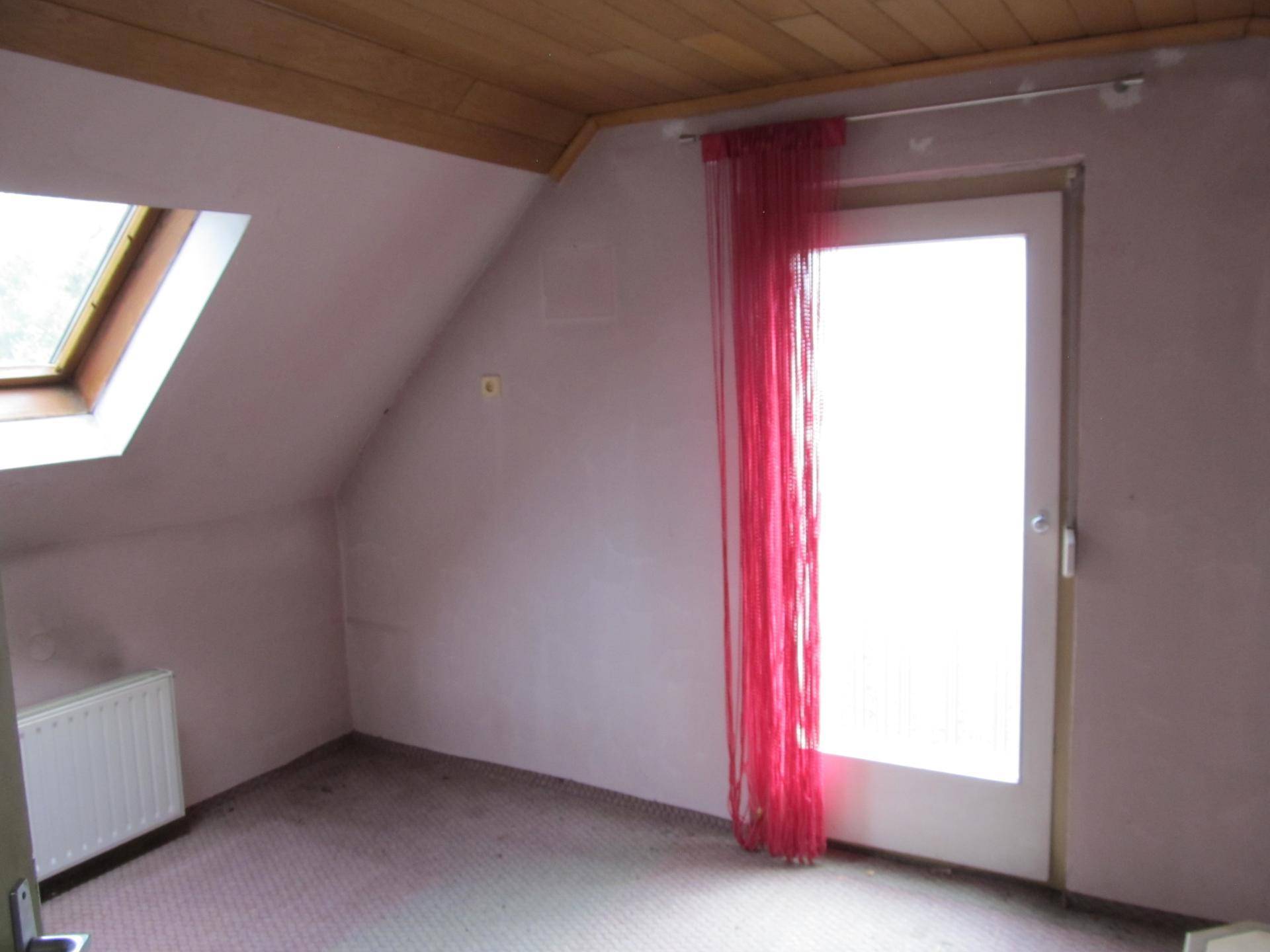 Dachzimmer mit schrägen Wänden, Dachfenster, Teppichboden und Zugang zu einem Balkon oder einer Terrasse.