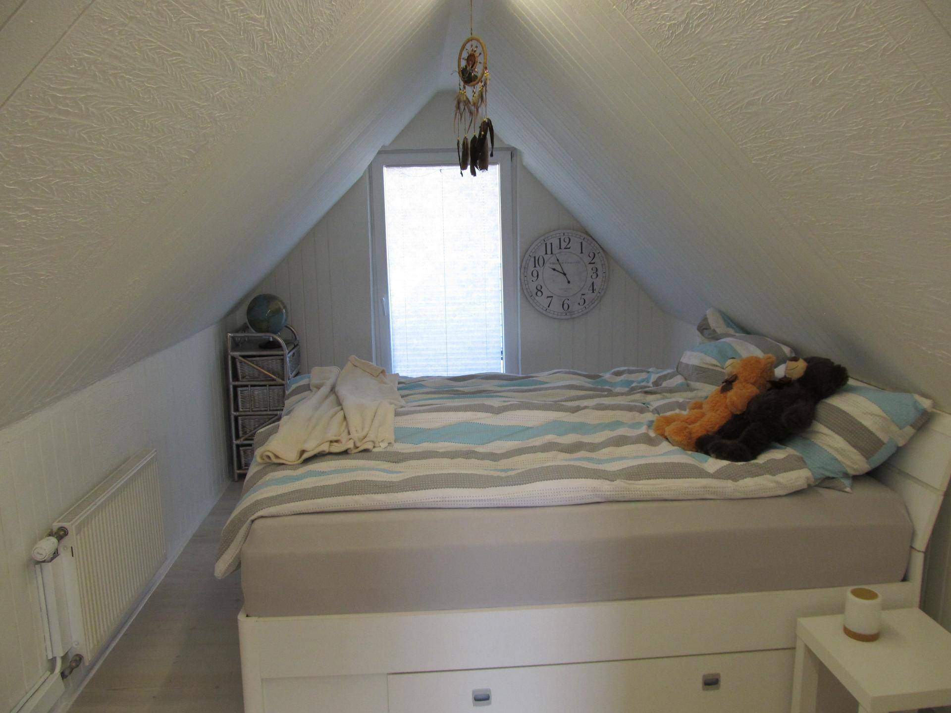 Gemütliches Schlafzimmer im Dachgeschoss mit schrägen Wänden und Fenster.
