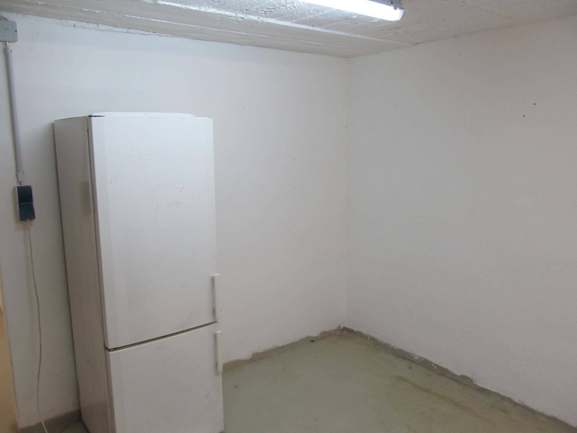 Einfacher Kellerraum mit einem Kühlschrank und viel Stauraum, ideal für Vorräte oder Lagerung.