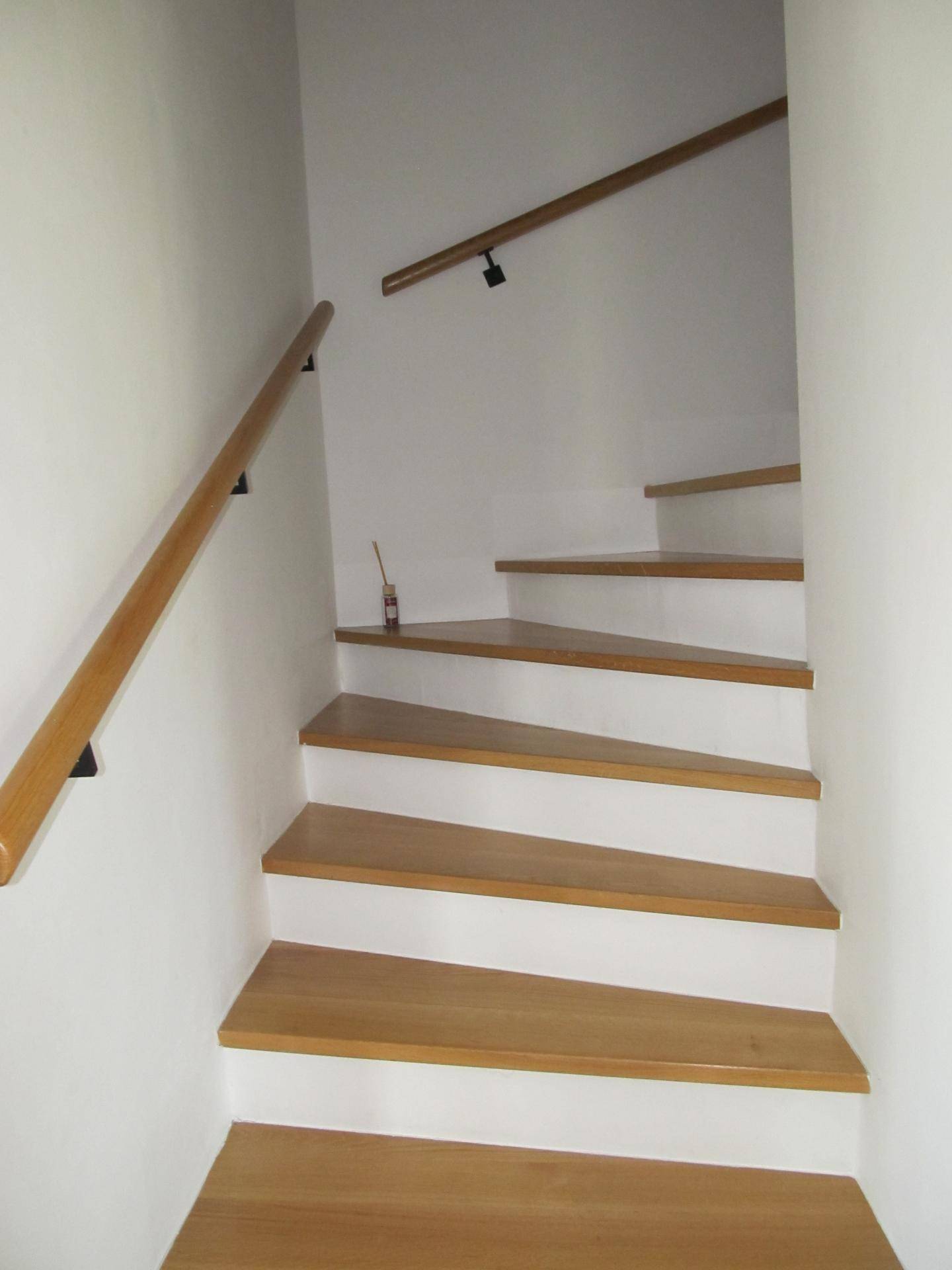Holztreppe mit hellem Geländer, die die verschiedenen Etagen des Hauses verbindet.