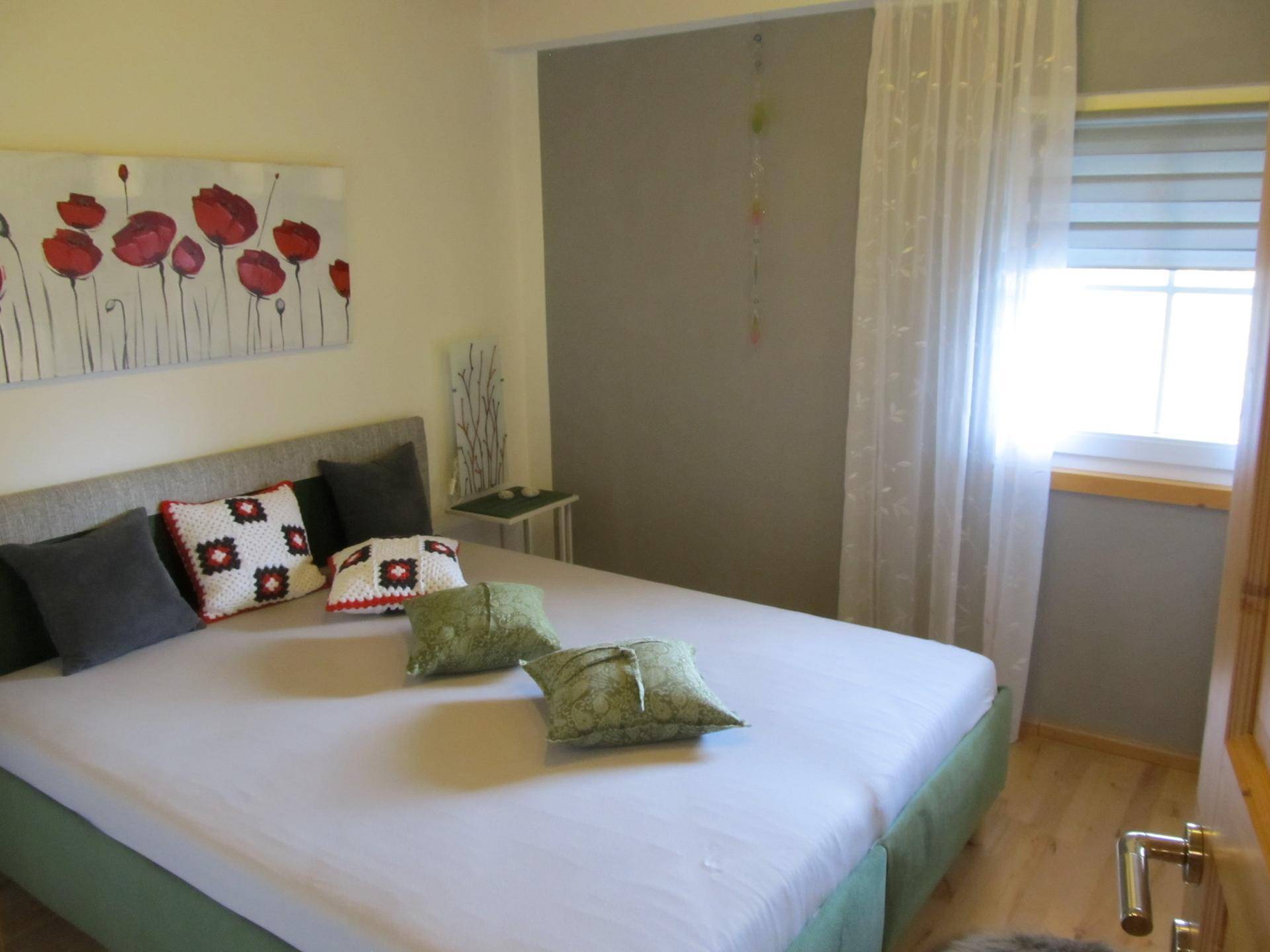 Schlafzimmer mit großem Bett, Holzboden und grünen Akzenten.