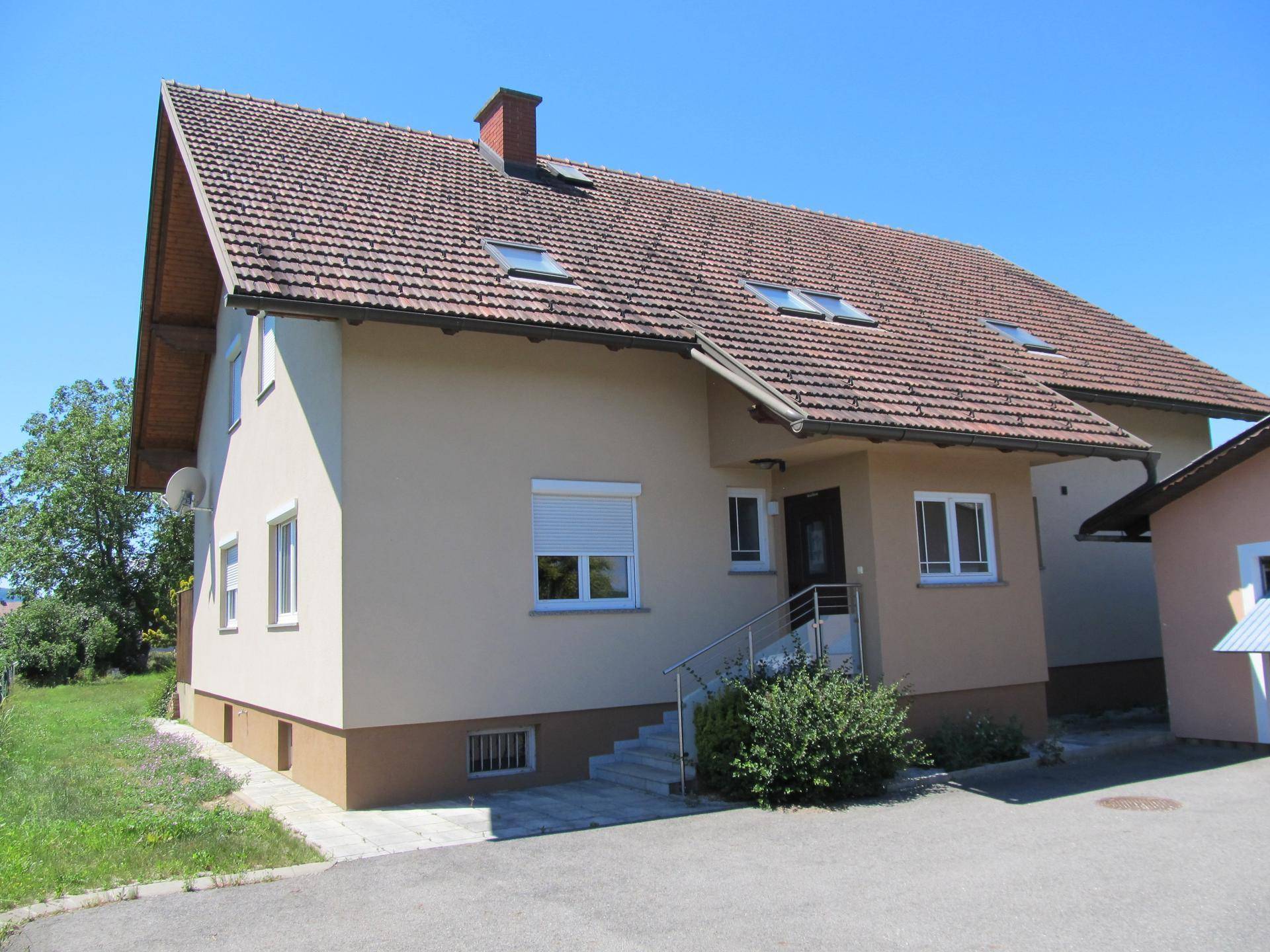 Vorderansicht des Hauses mit Eingangsbereich, Treppe und gepflasterter Zufahrt unter klarem Himmel.