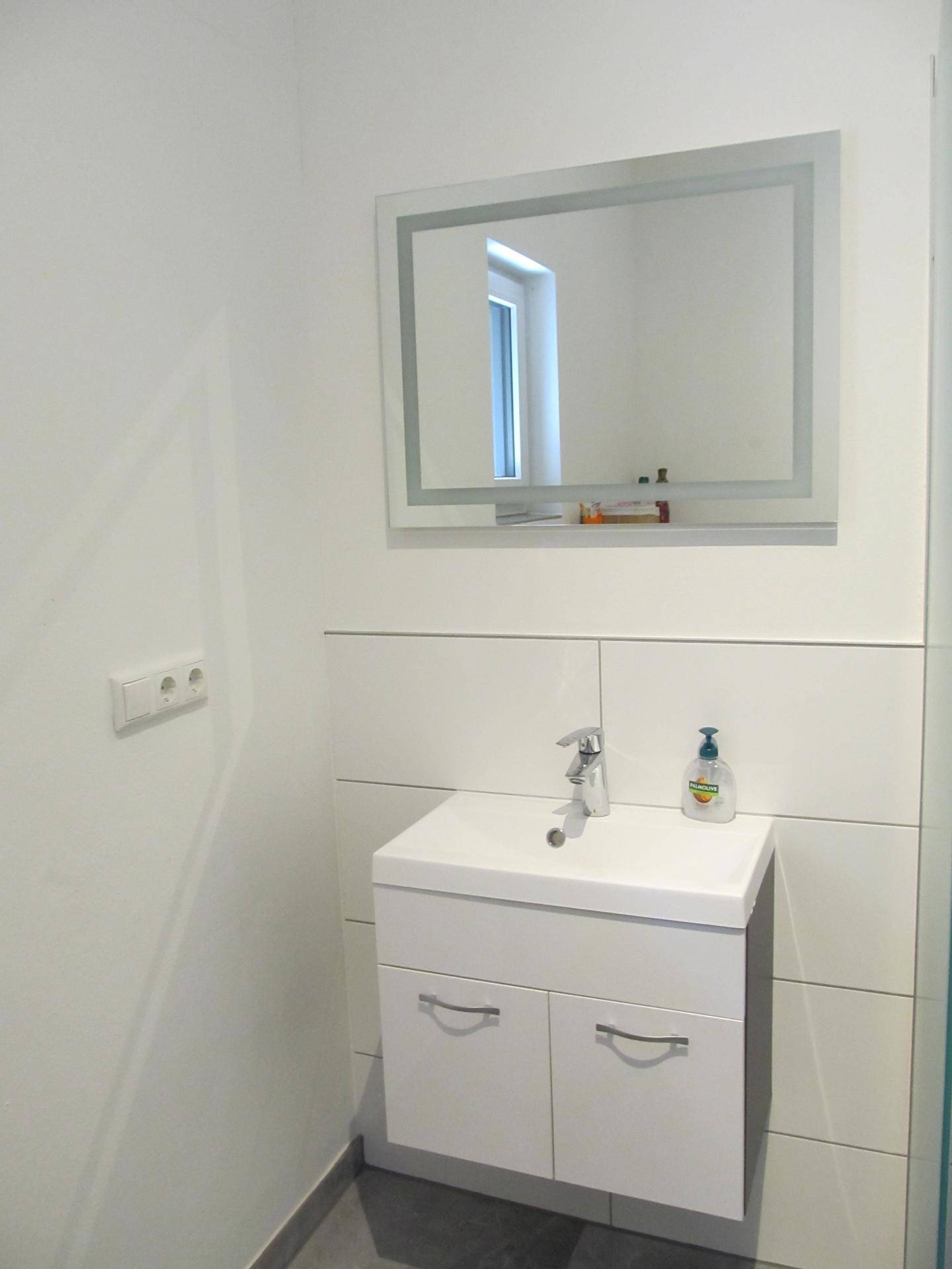 Modernes Badezimmer mit weißem Waschtischunterschrank, Spiegel und hellen Fliesen an der Wand.