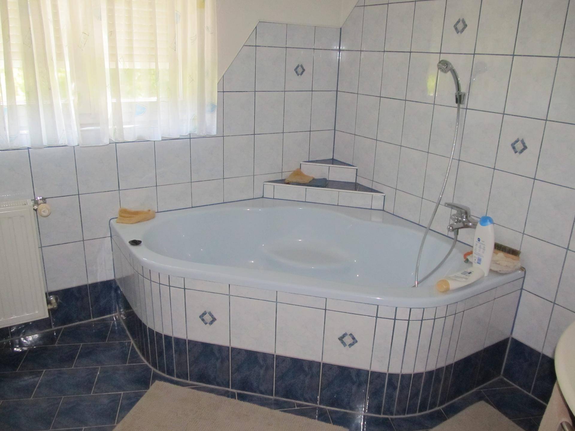 Badezimmer mit Eckbadewanne, blauen und weißen Fliesen und Fenster für Tageslicht.