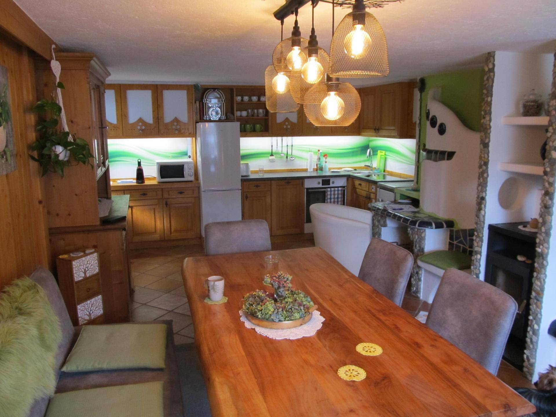 Offener Wohn- und Essbereich mit großer Holztafel und traditionellem Kachelofen.