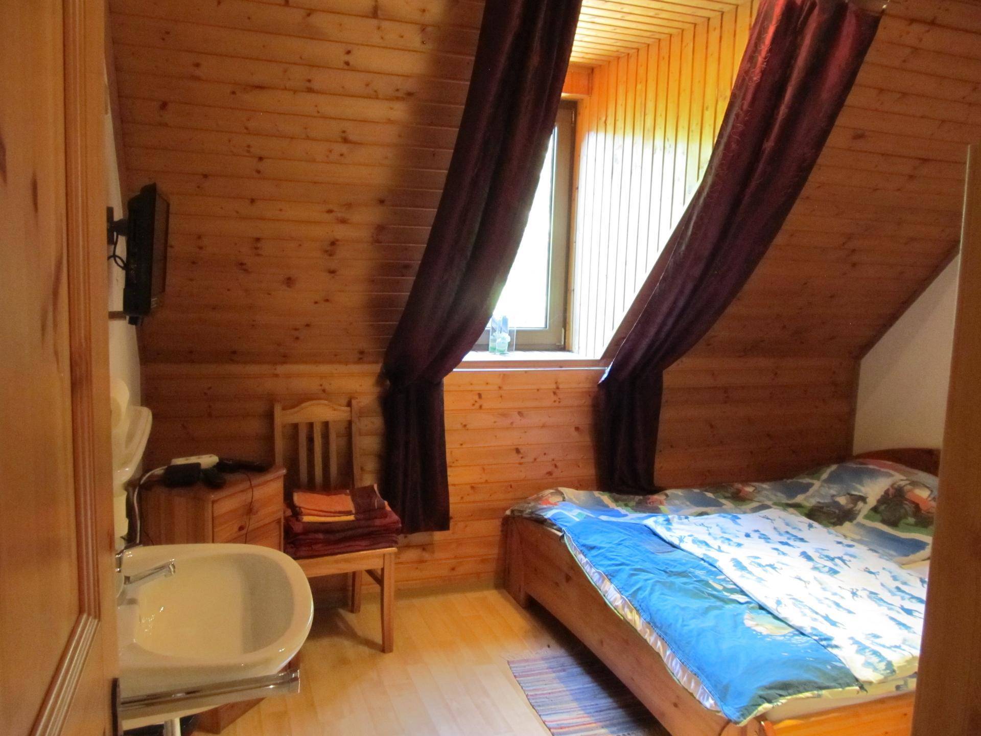 Gemütliches Schlafzimmer im Dachgeschoss mit Holzverkleidung, Bett und Waschbecken.