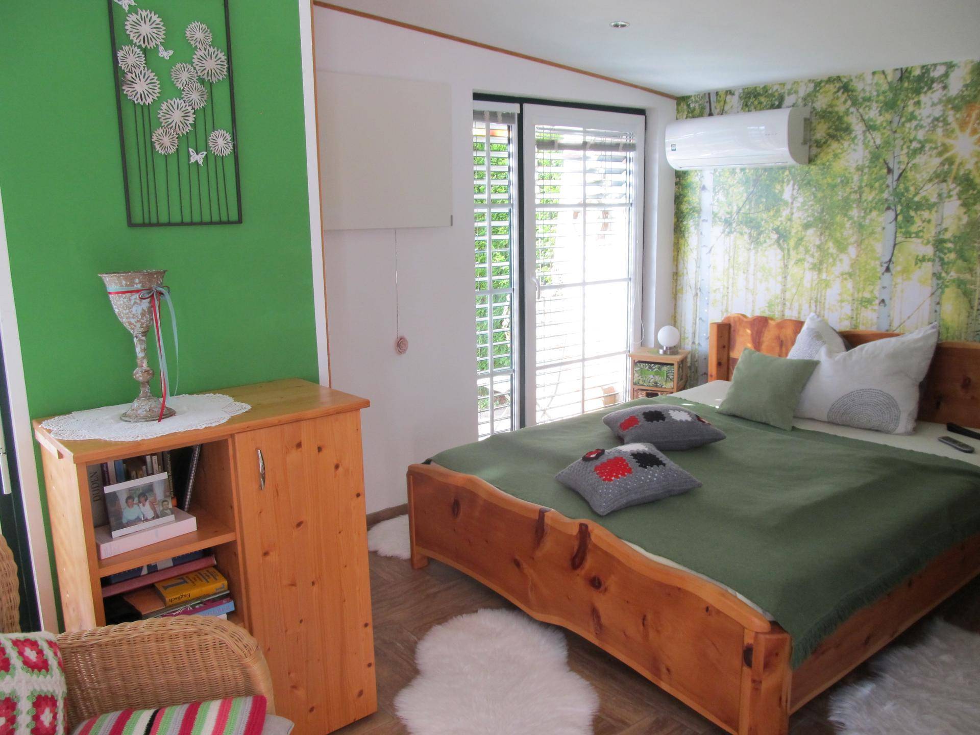 Schlafzimmer mit Holzbett, grüner Wand und Klimaanlage.