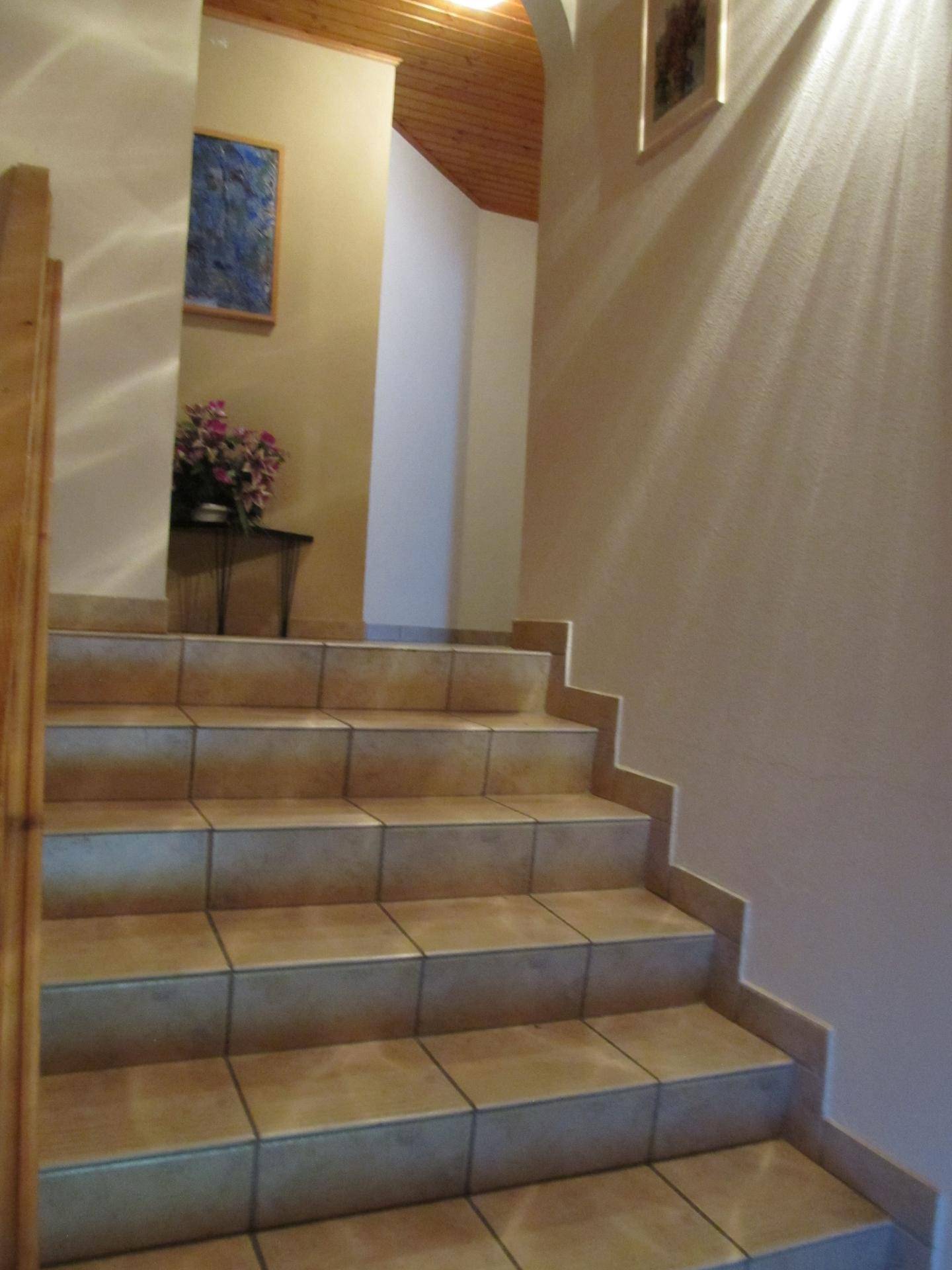 Heller Treppenaufgang mit Fliesenboden und Holzdecke, führt in die obere Etage.