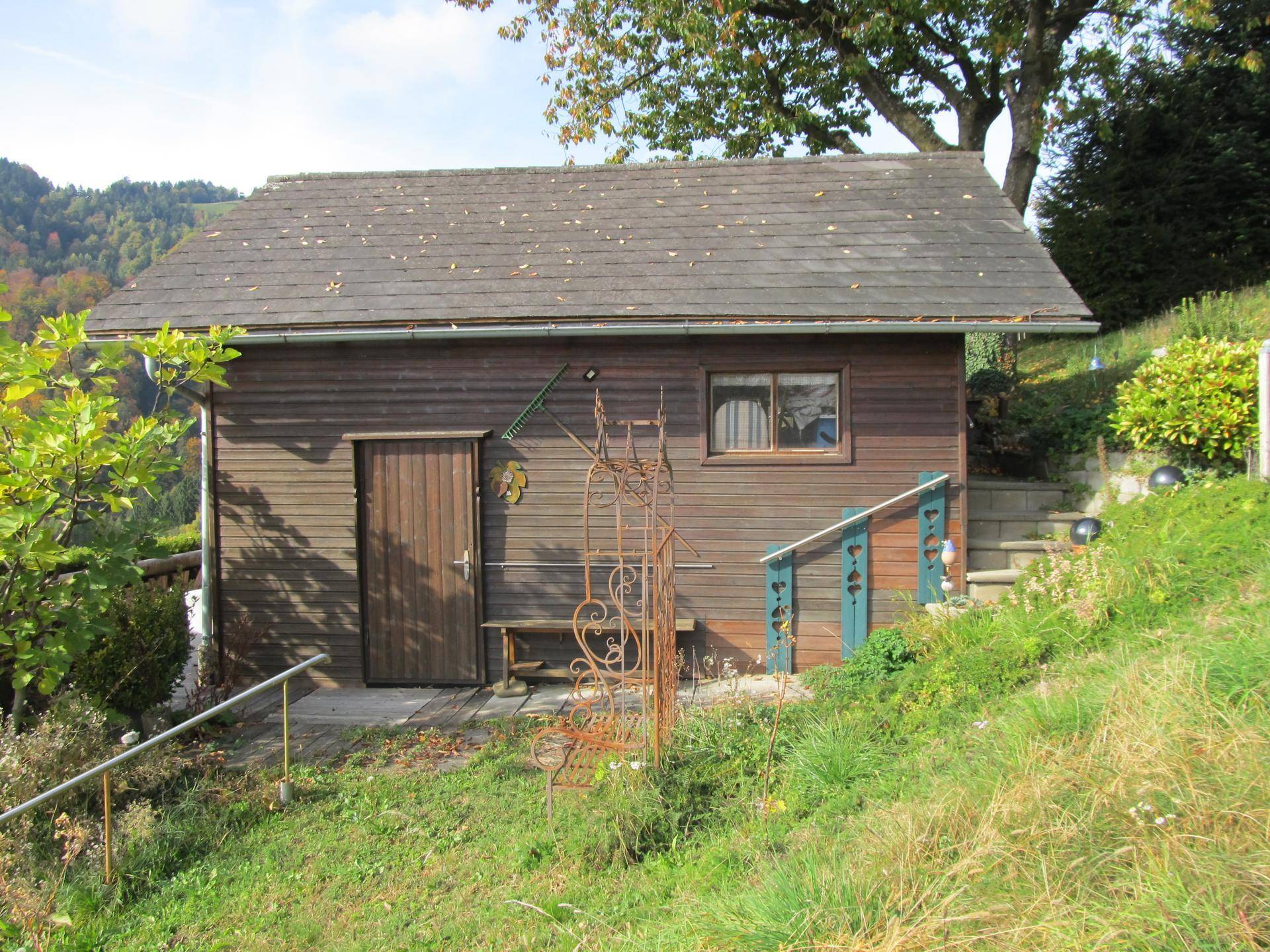 Seitenansicht der Holzhütte mit Holztür und Fenster, umgeben von Grün.