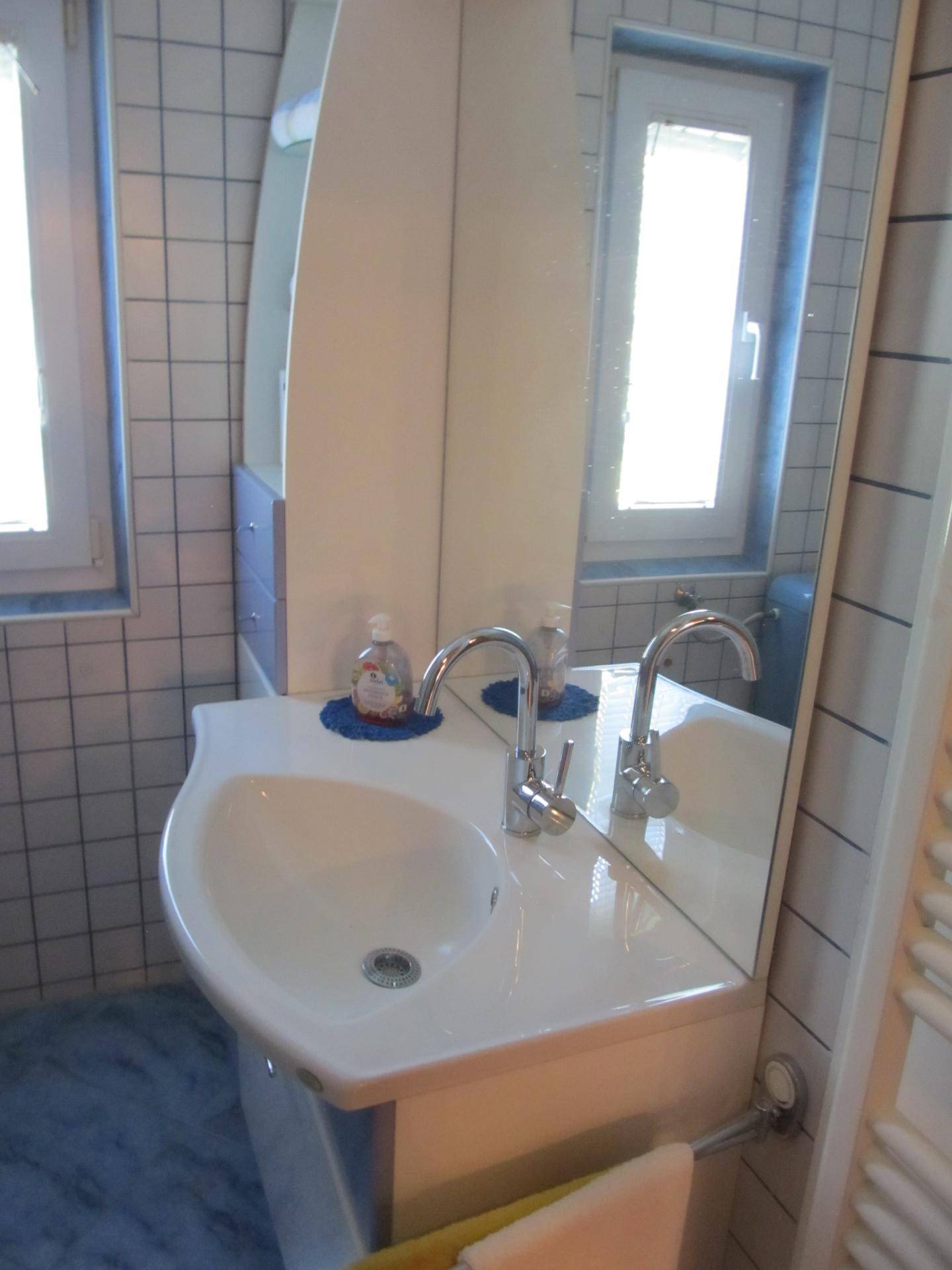 Badezimmer mit einem einzelnen Waschbecken, großem Spiegel und weißen Fliesen.