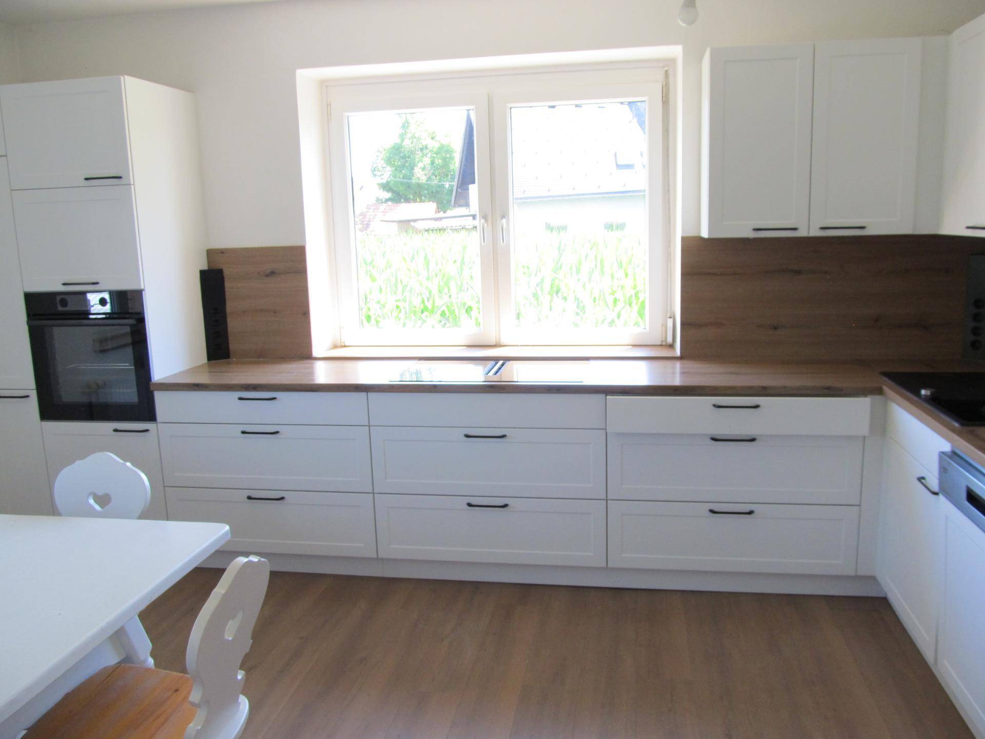 Helle, moderne Küche mit weißen Schränken, Holz-Arbeitsplatten und Fenster mit Blick ins Grüne.
