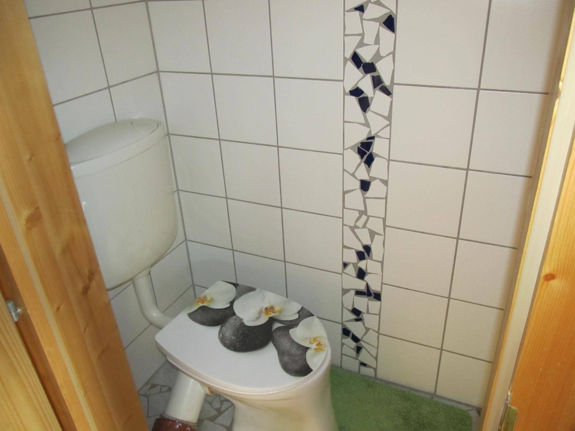 Kleine Gästetoilette mit weißen Fliesen und einem dekorativen Mosaikstreifen.