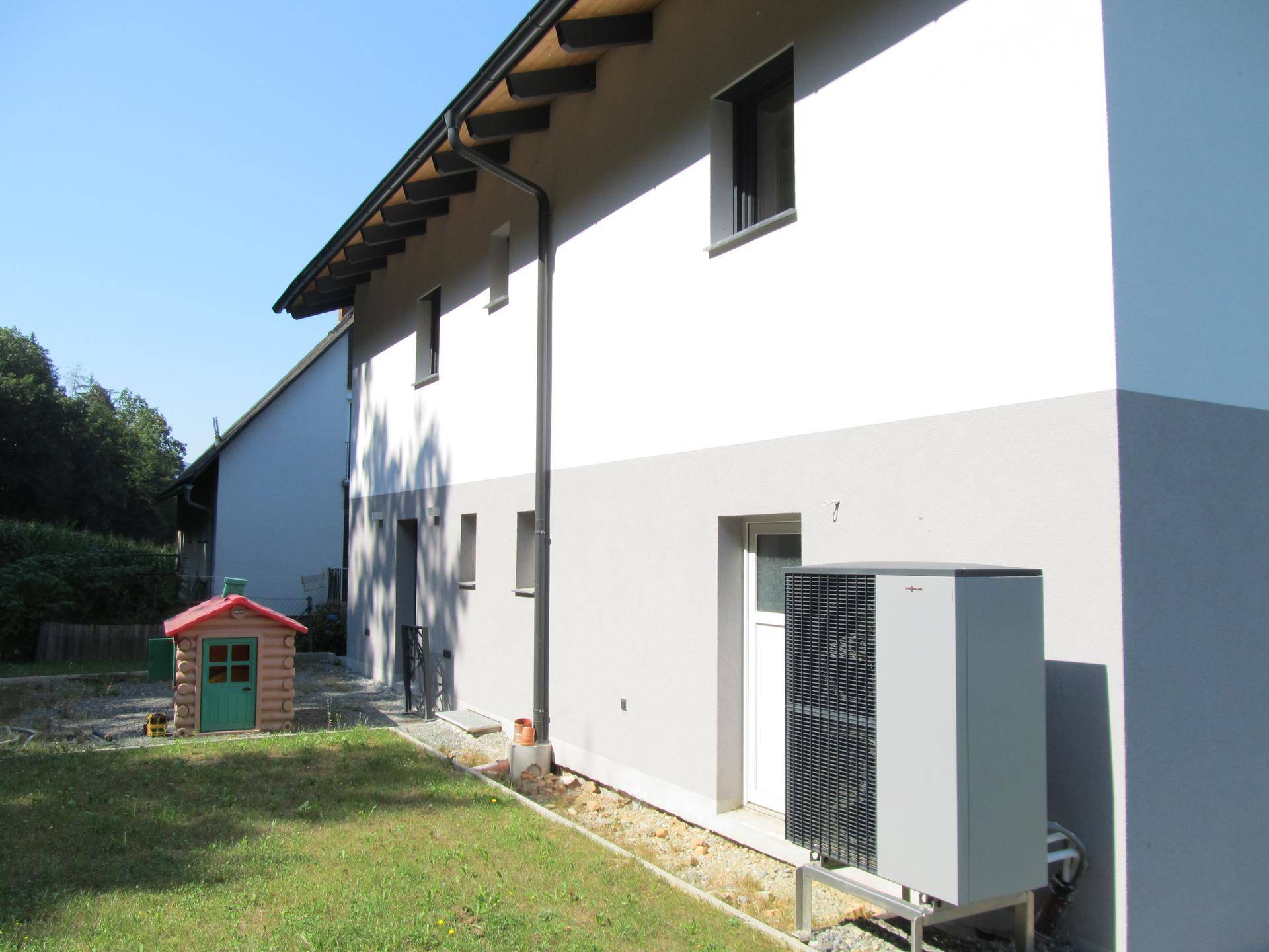 Seitenansicht des Hauses mit Wärmepumpe und einem kleinen Spielhaus im Garten.