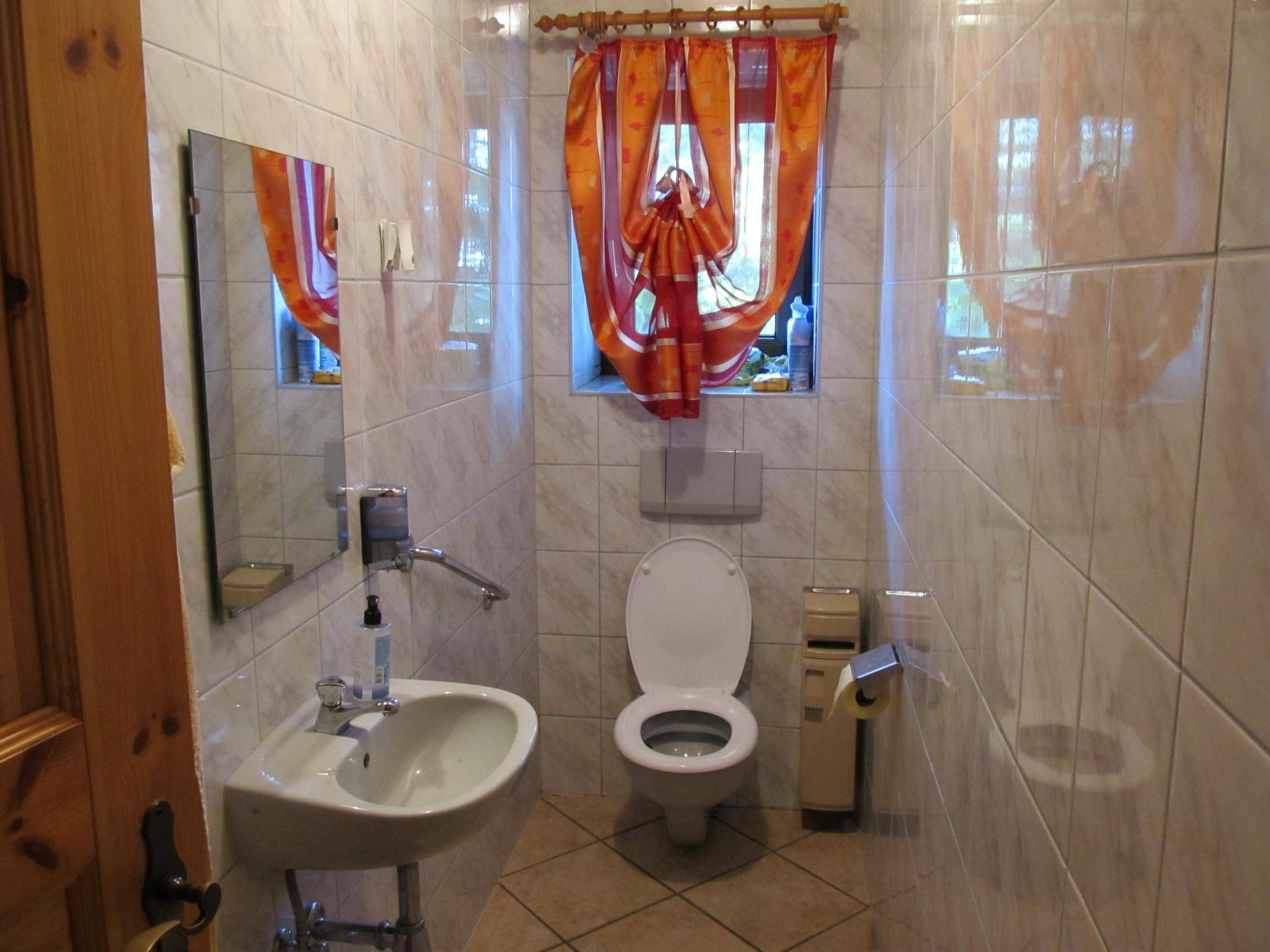 Separate Gästetoilette mit Waschbecken, WC und hellen Fliesen, mit Fenster.