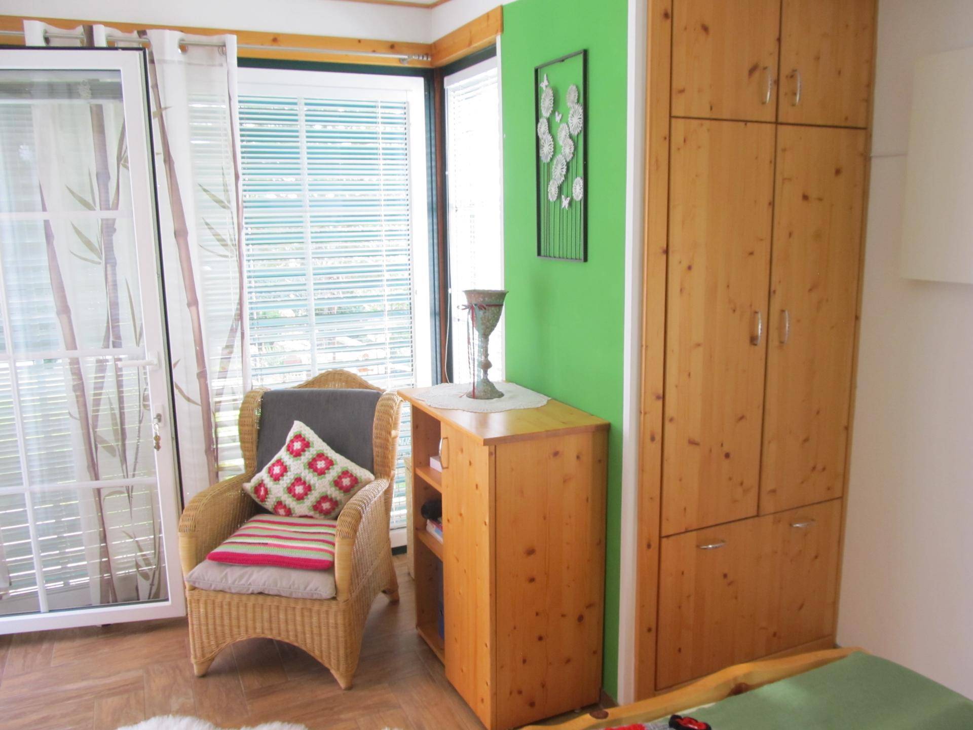 Schlafzimmer mit eingebautem Holzschrank, Korbsessel und großem Fenster.