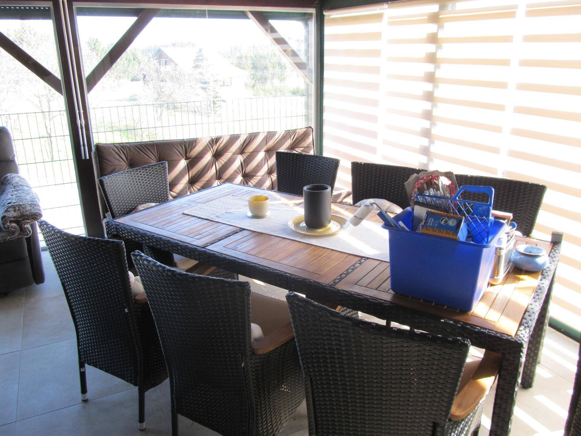 Heller Essbereich im Wintergarten mit Rattanmöbeln und Jalousien.