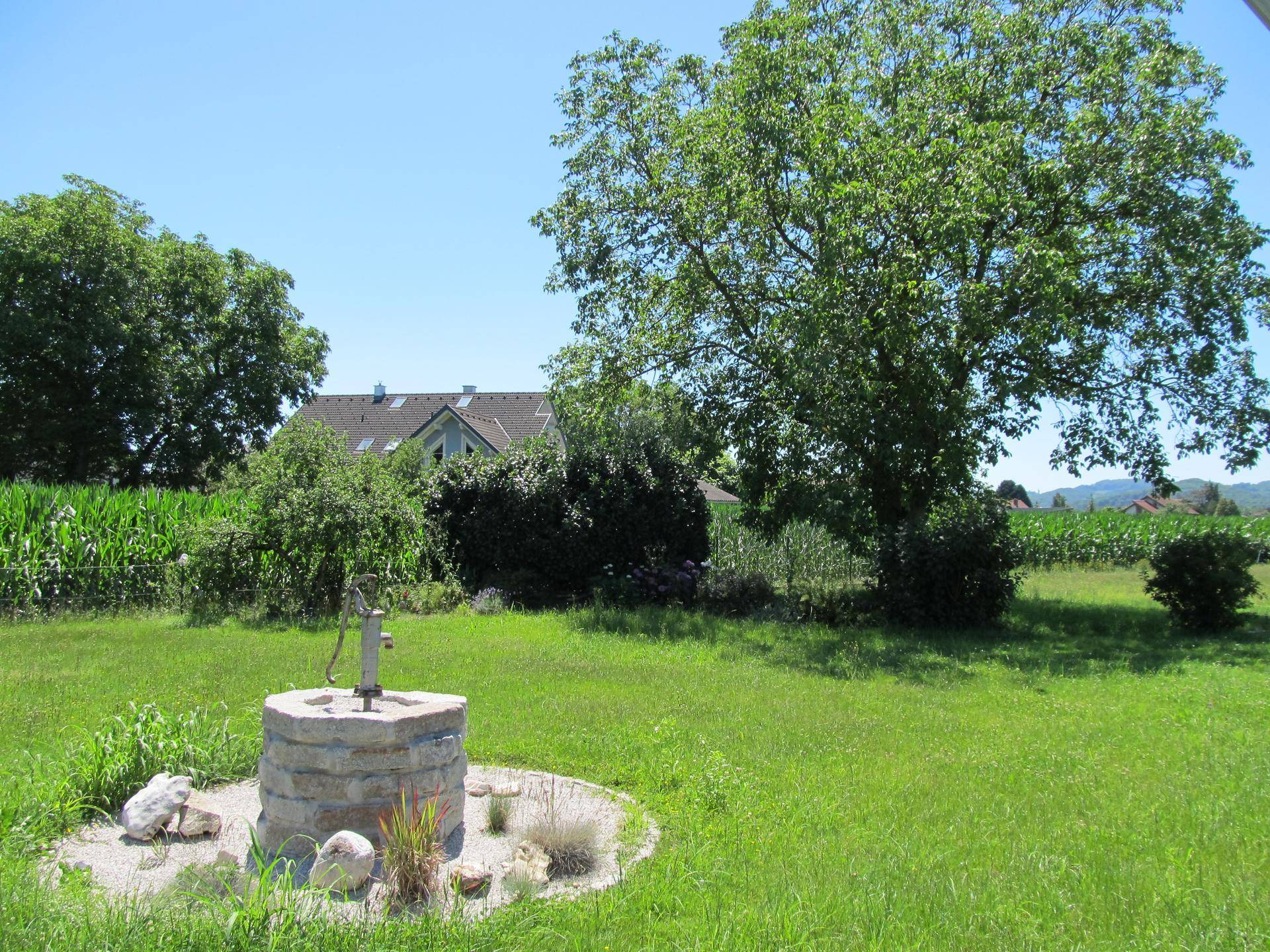 Idyllischer Gartenbereich mit Zierbrunnen, alten Bäumen und weitem Blick auf die Landschaft.