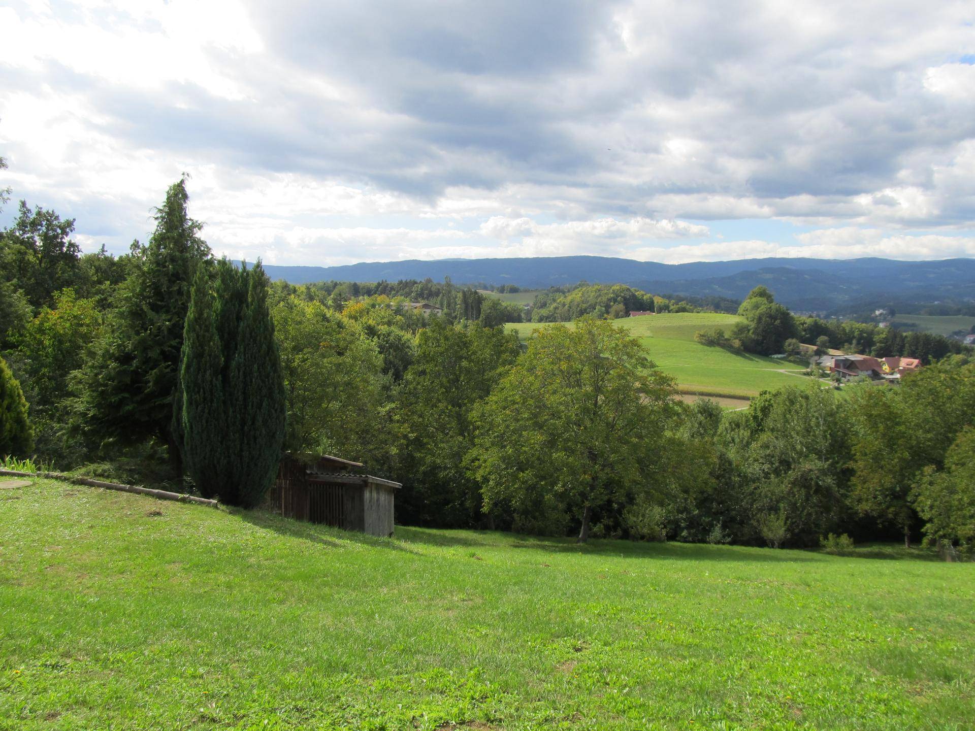 Malerische Landschaft mit grünen Wiesen, Wäldern und einem kleinen Holzschuppen, der sich harmonisch einfügt.