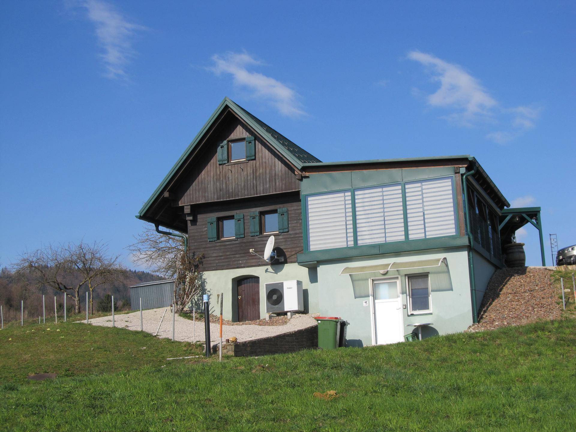 Wohnhaus mit grünem Dach und Anbau in ländlicher Umgebung unter blauem Himmel.