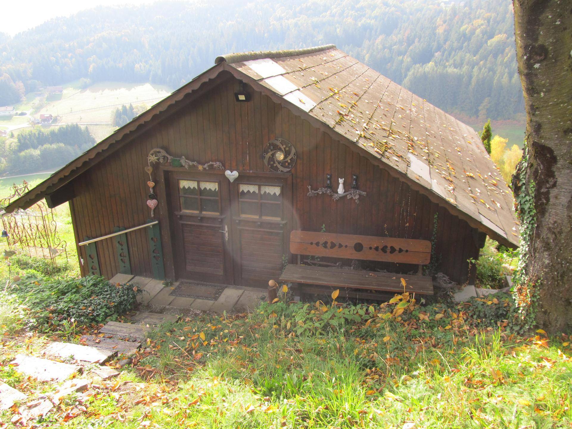 Rustikale Holzhütte mit Satteldach und einer Holzbank in ländlicher Umgebung.