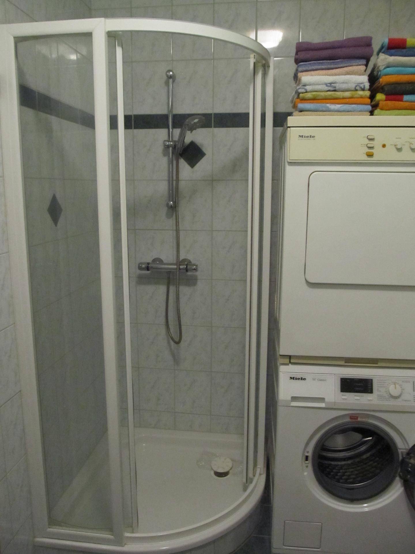 Badezimmer mit Duschkabine, Waschmaschine und Trockner, gefliest in hellen und dunklen Tönen.