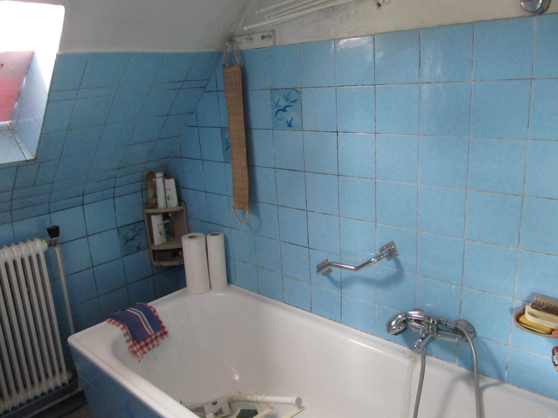 Badezimmer mit blauen Fliesen, Badewanne und Dachfenster in einem Raum mit schrägen Wänden.