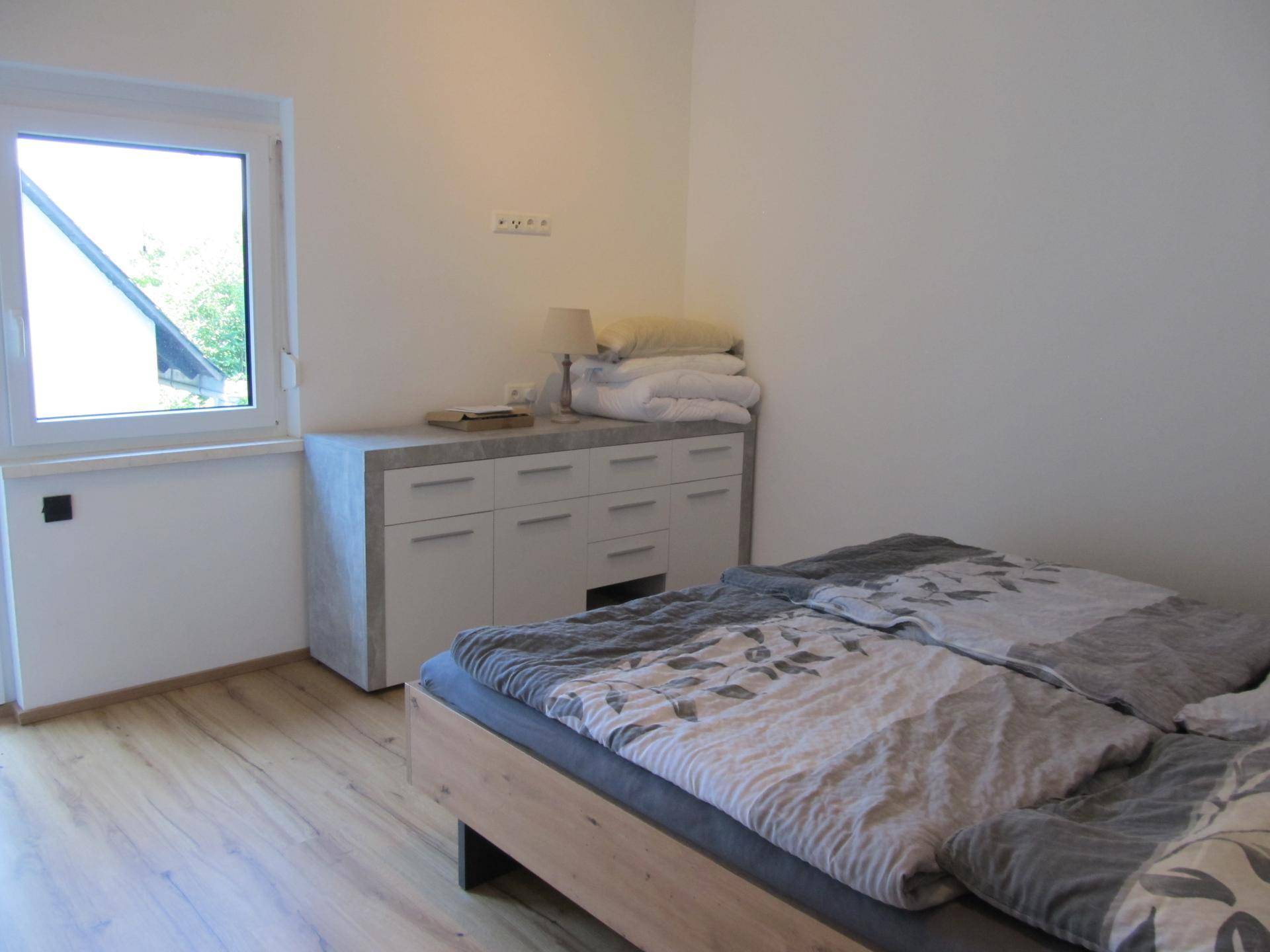 Schlafzimmer mit Doppelbett, Kommode und Fenster mit Blick nach draußen.