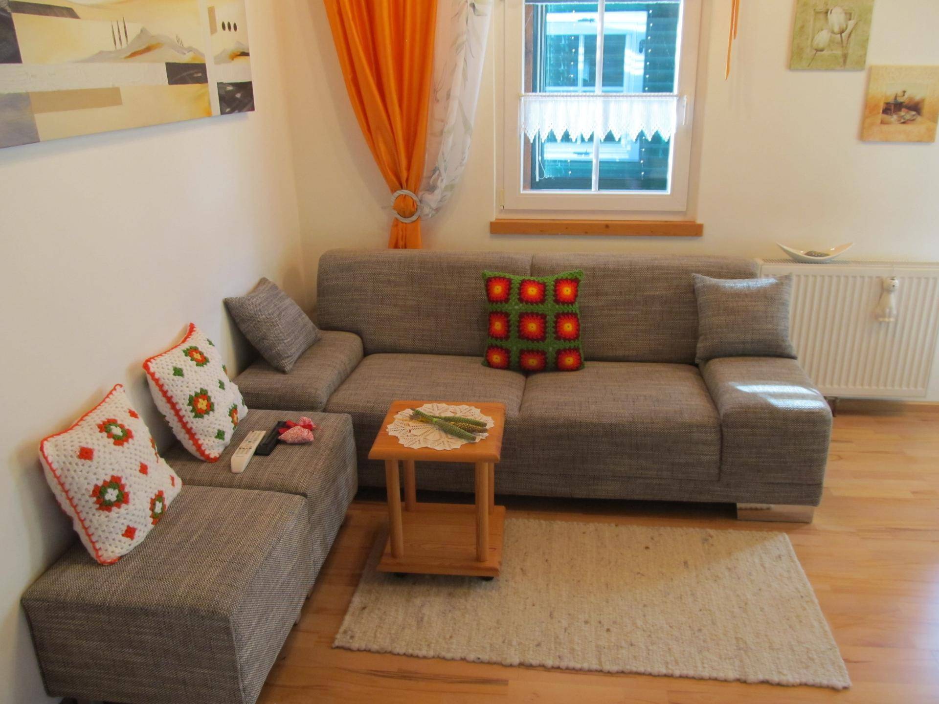 Gemütliches Wohnzimmer mit Sofa, Holzboden und einem Fenster mit Vorhängen.