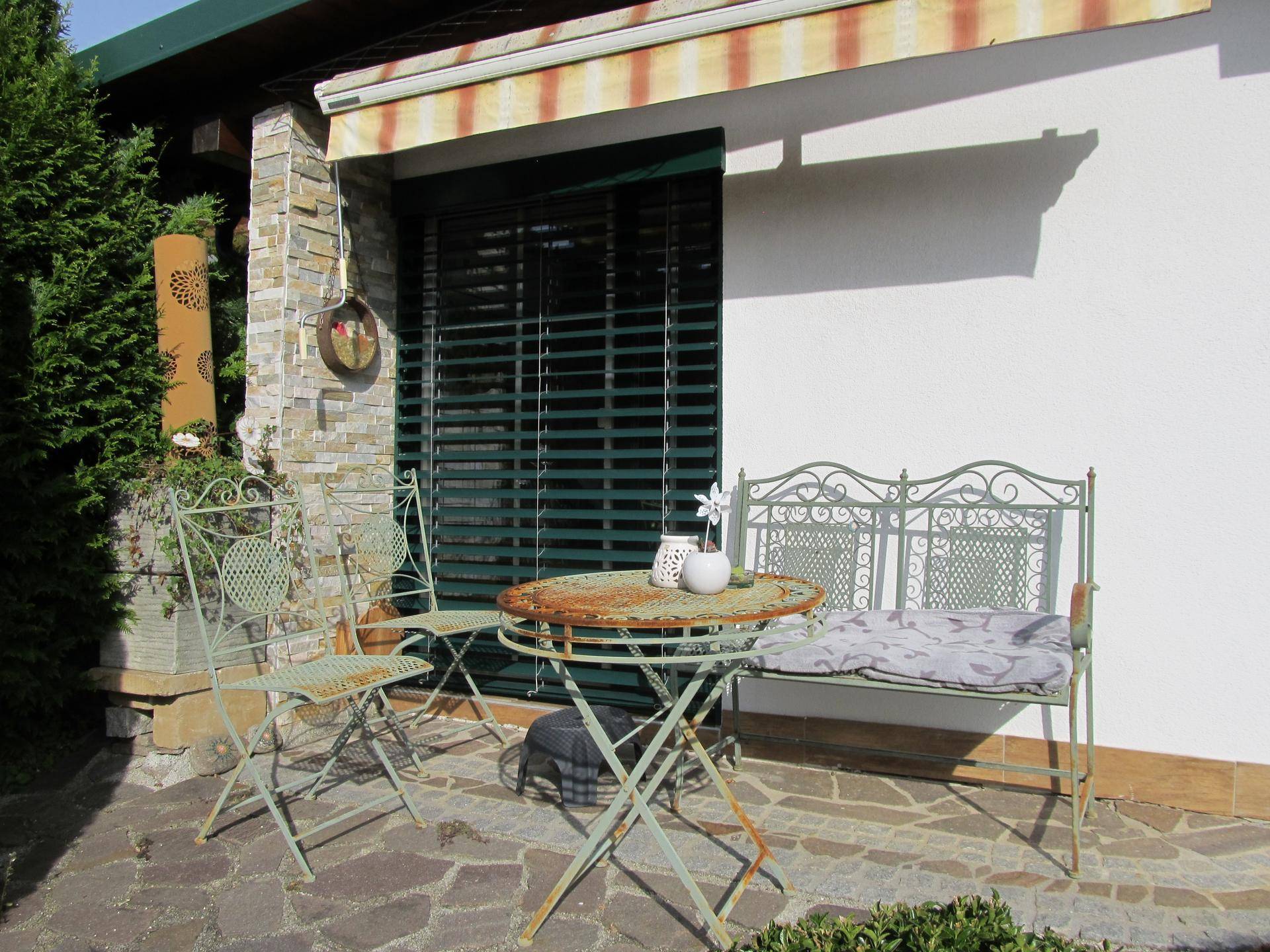Kleine Terrasse mit schmiedeeisernen Gartenmöbeln und einer Markise am Haus.