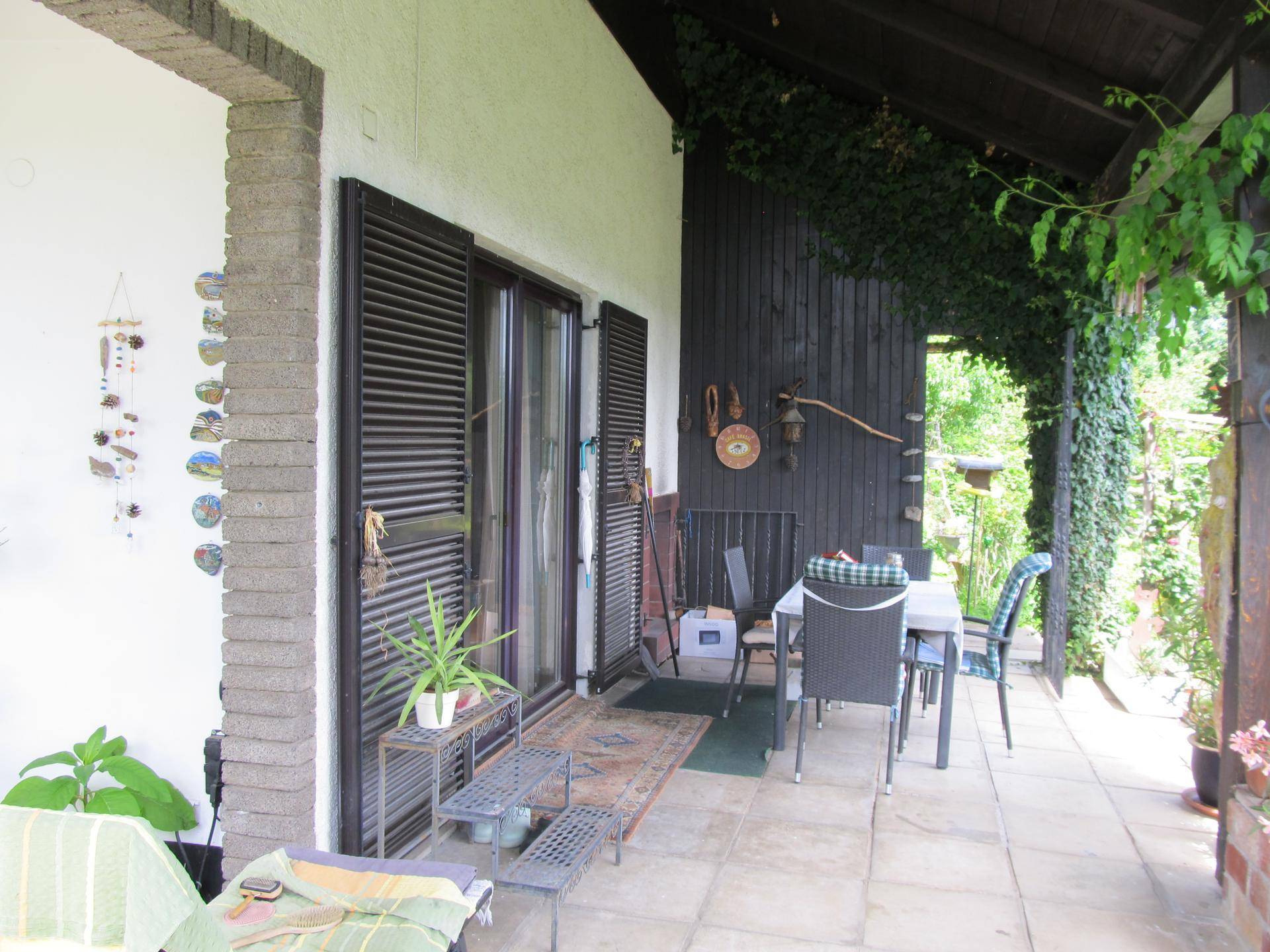 Geräumige Terrasse mit Esstisch, Stühlen und Zugang zum Haus, umgeben von viel Grün.