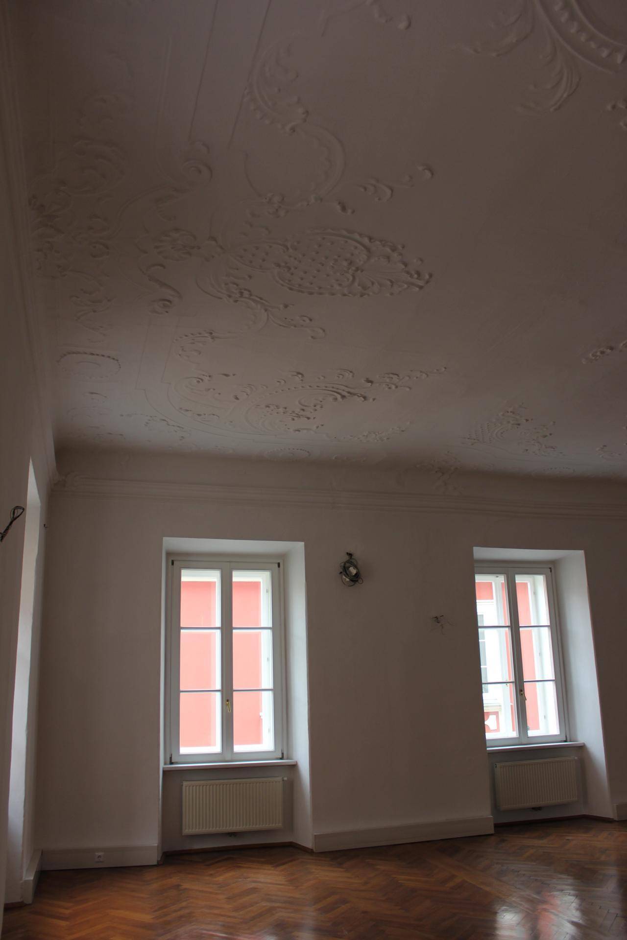 Detailansicht der hohen Decke mit aufwendigen Stuckverzierungen und großen Fenstern, die viel Tageslicht hereinlassen.