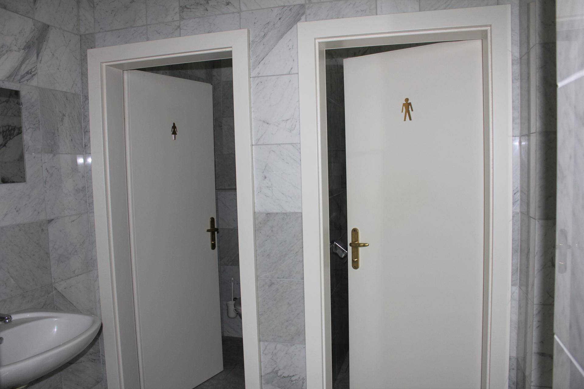 Zwei separate Toilettenkabinen mit Marmorfliesen und Waschbecken, geeignet für gewerbliche Nutzung im Gebäude.