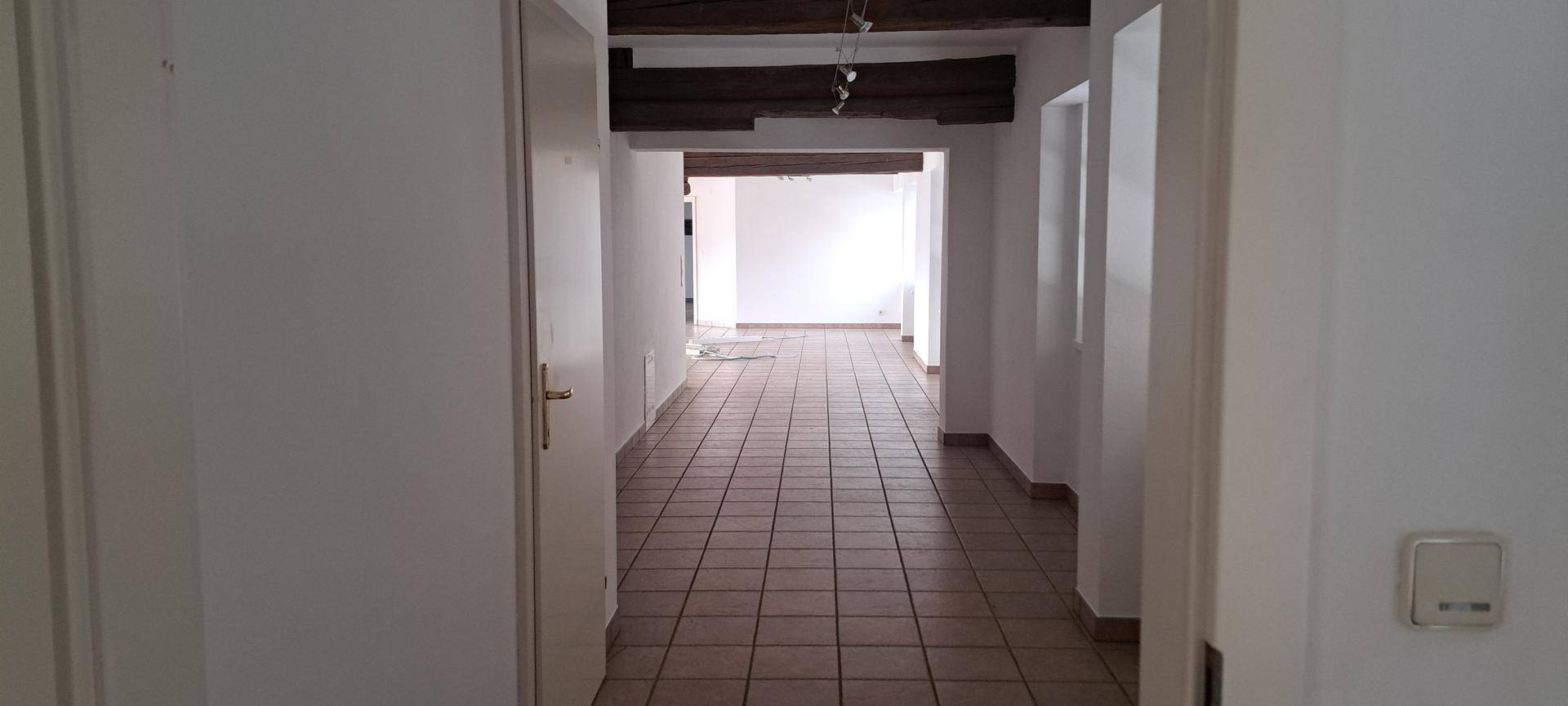 Langer Flur mit Fliesenboden und Holzbalken, der zu weiteren Räumen im Gebäude führt.