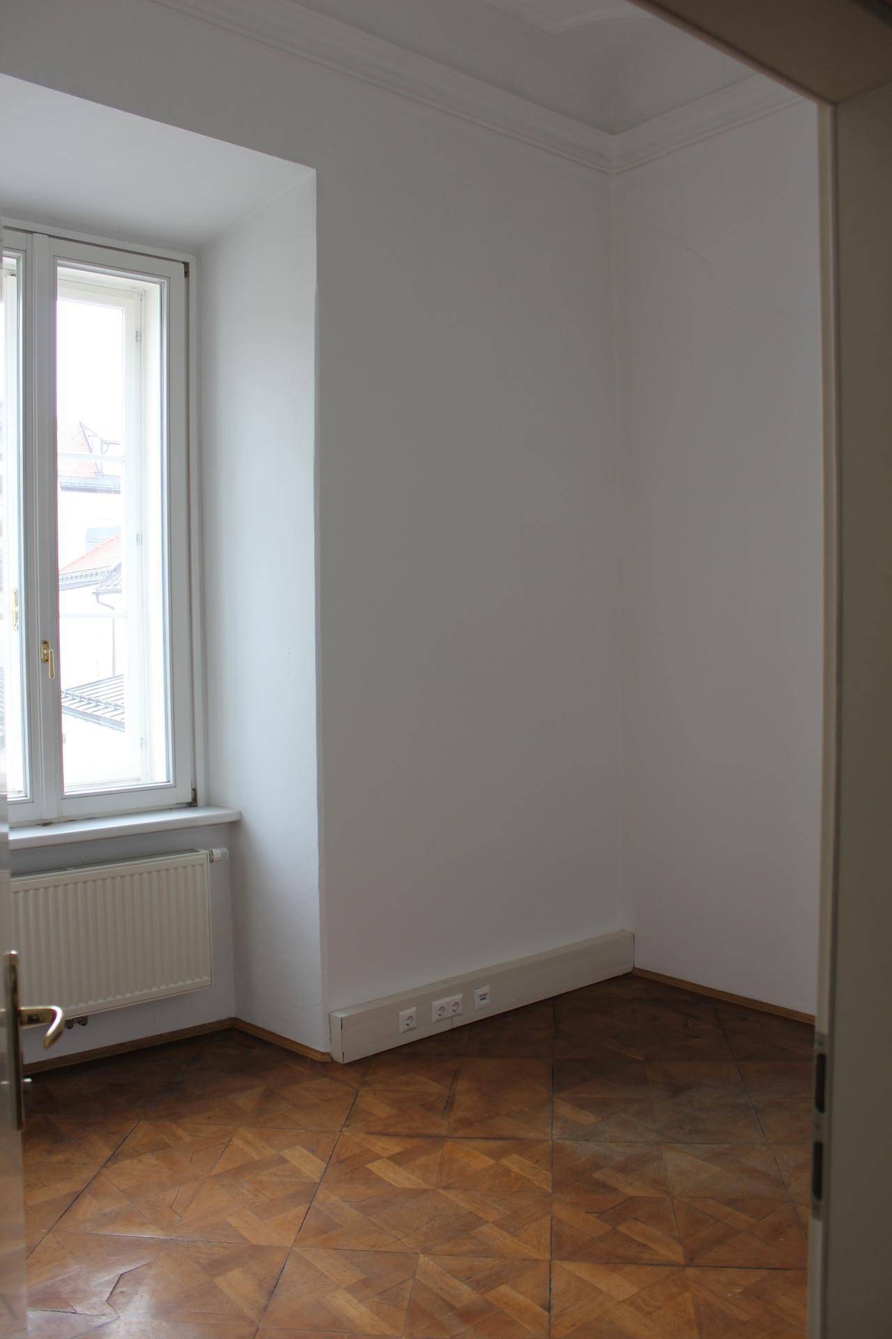 Heller Büroraum mit Parkettboden und großem Fenster, das viel natürliches Licht bietet, ideal als Arbeitsplatz.