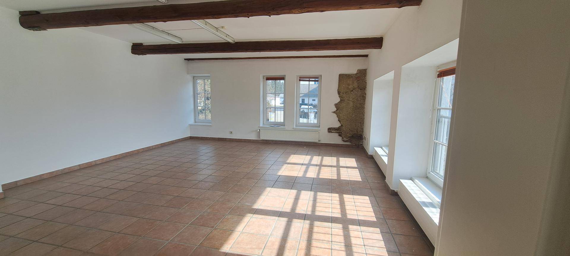 Großer, leerer Raum mit Terrakottafliesen, sichtbaren Holzbalken und viel Tageslicht.