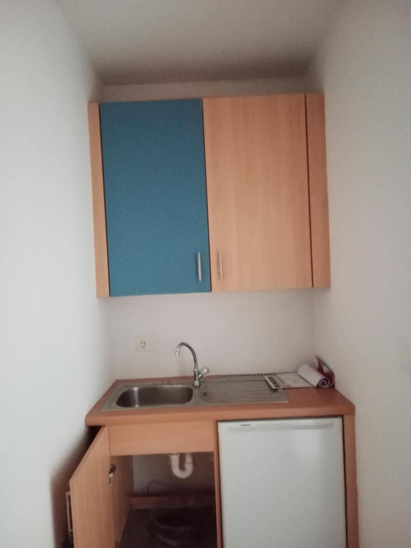Kompakte Küchenzeile mit Spüle, Kühlschrank und Hängeschränken in Holz- und Blautönen, praktisch und funktional.