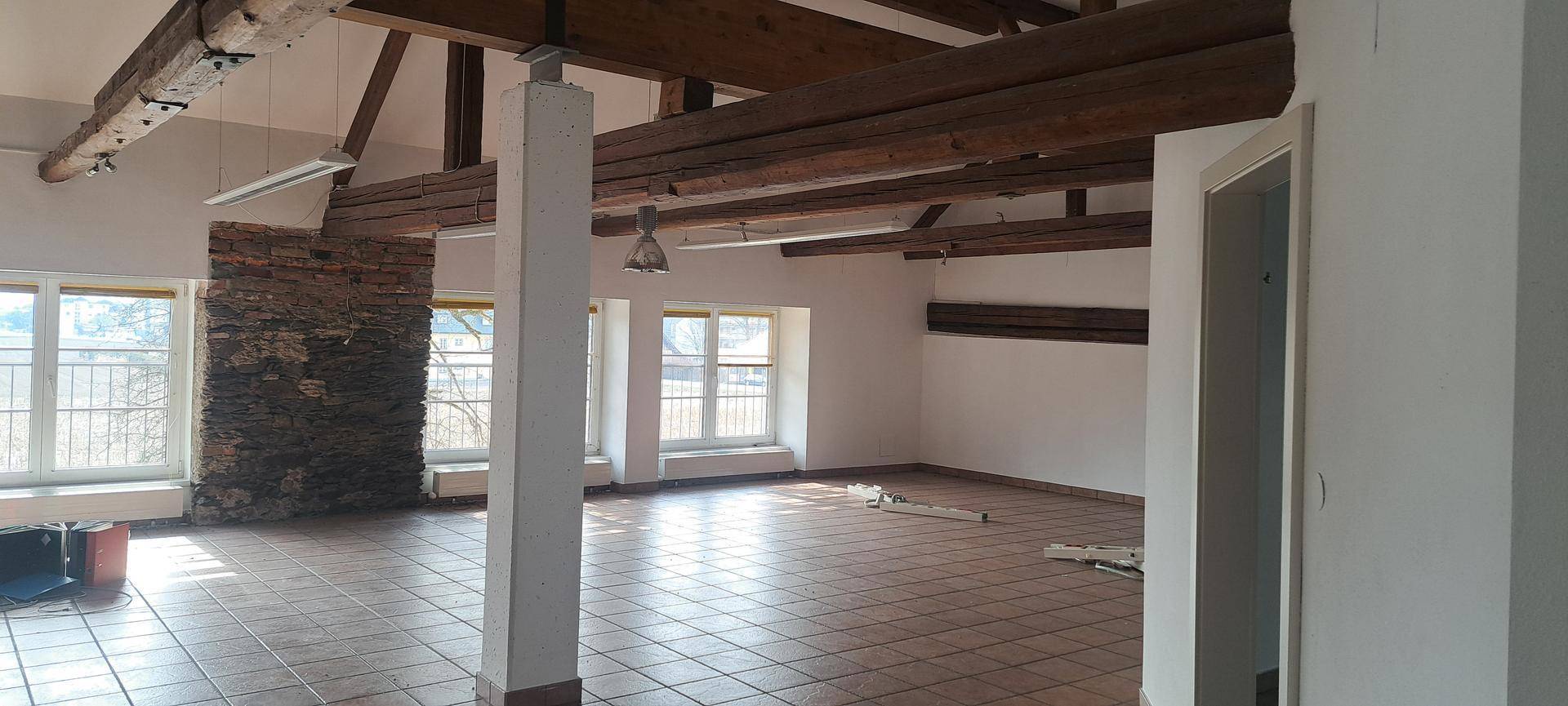 Heller Büroraum mit Holzbalken, Fliesenboden und einer rustikalen Steinwand als Akzent.