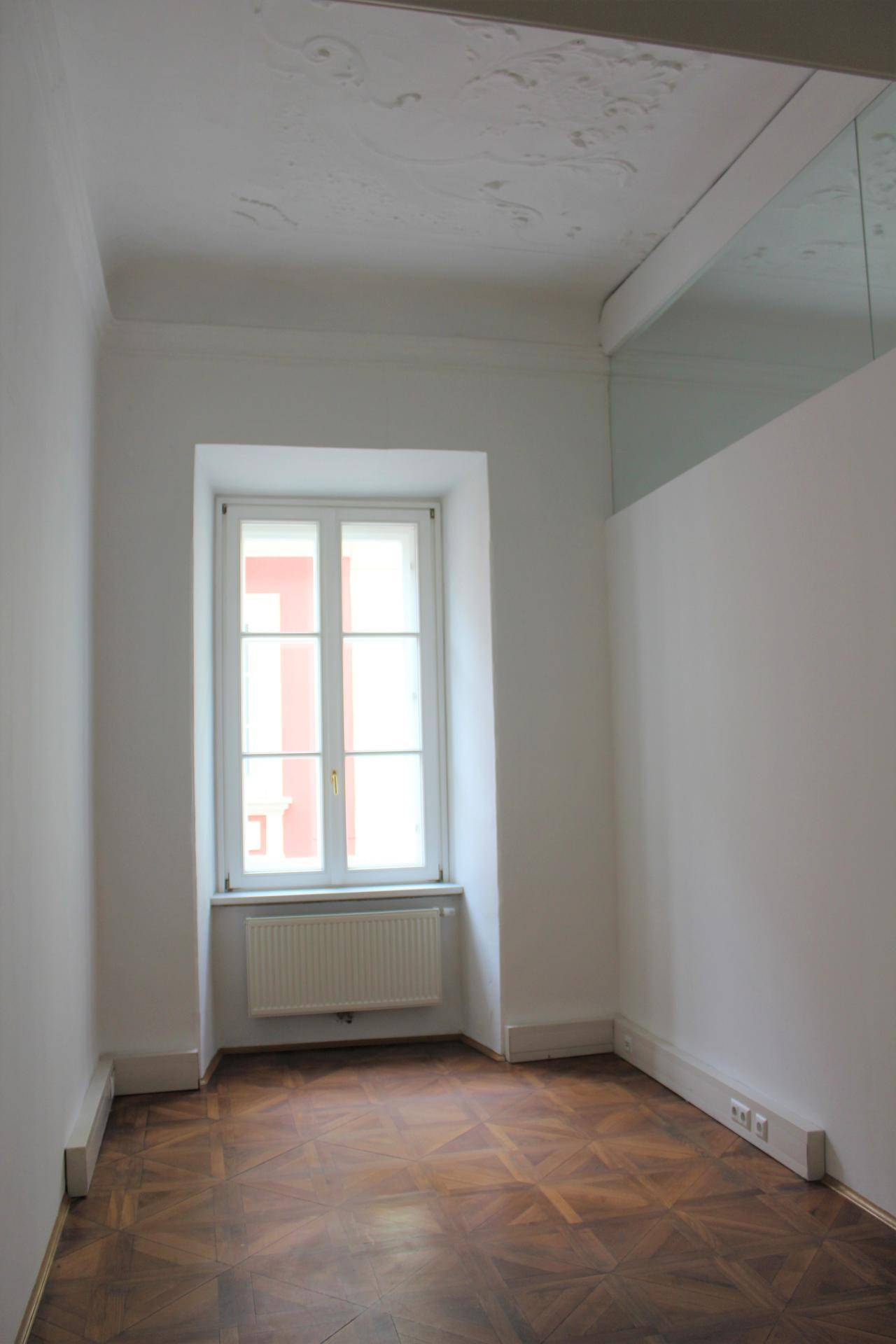 Heller, kleiner Büroraum mit Parkettboden und einem Fenster, das Tageslicht hereinlässt, ideal als Einzelbüro.