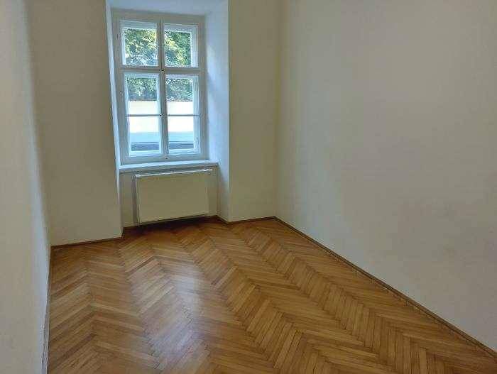 Helles Zimmer mit klassischem Fischgrätparkett, Fenster und Heizkörper, einladend gestaltet.