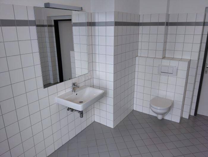 Separates WC mit Waschbecken, Spiegel und weißen Fliesen an den Wänden.